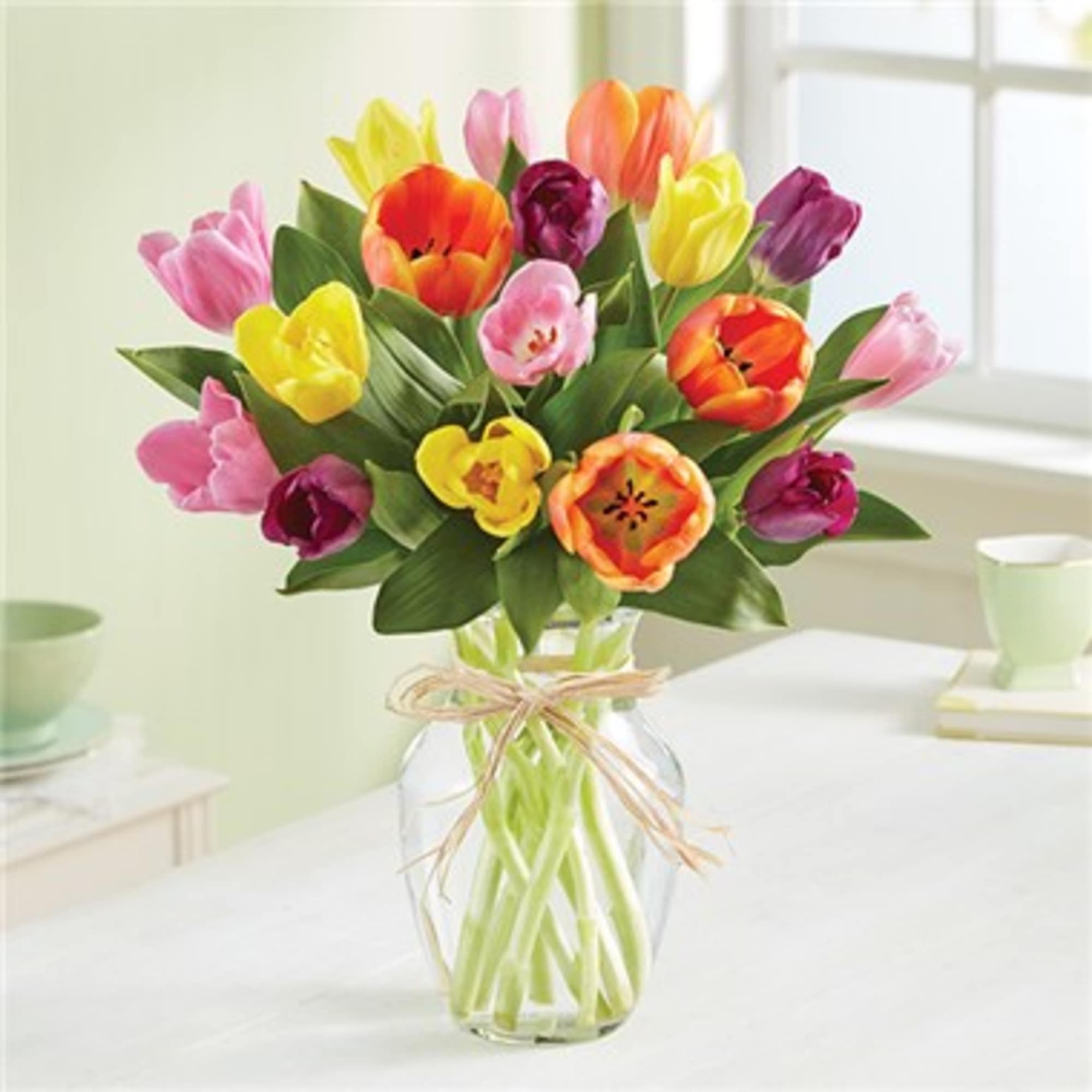 Mixed-color tulip bouquet in a clear glass vase tied with twine on a light table.