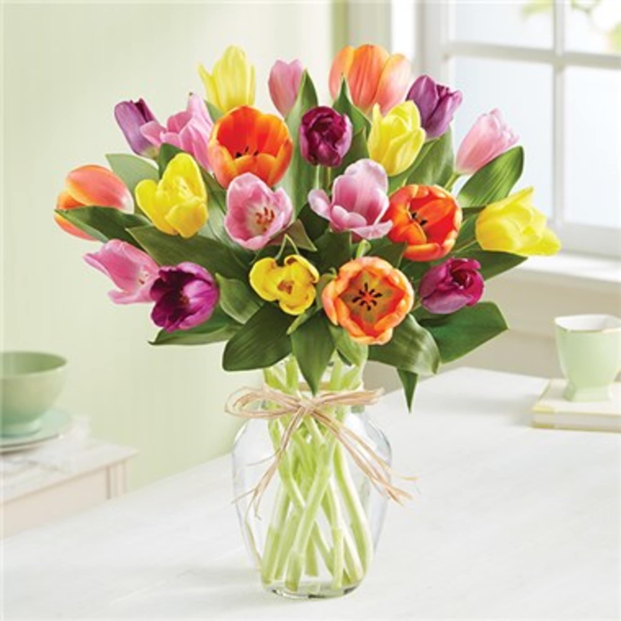 Mixed tulip bouquet in bright colors arranged in a clear glass vase with a twine bow.