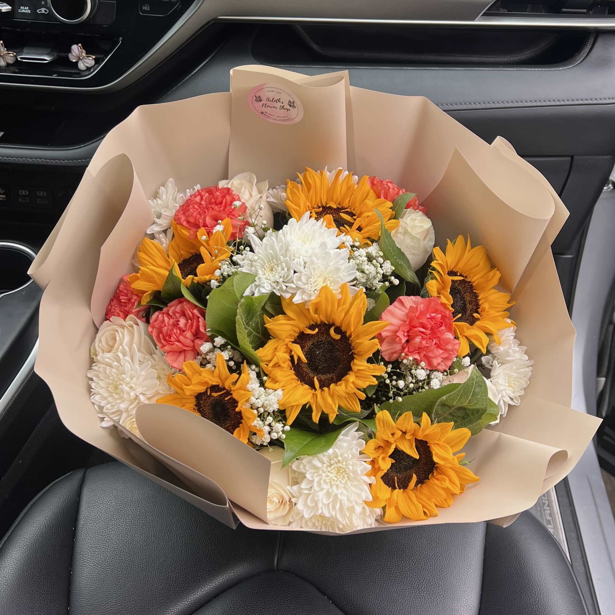 Bouquet of sunflowers, white blooms, and pink carnations wrapped in beige paper
