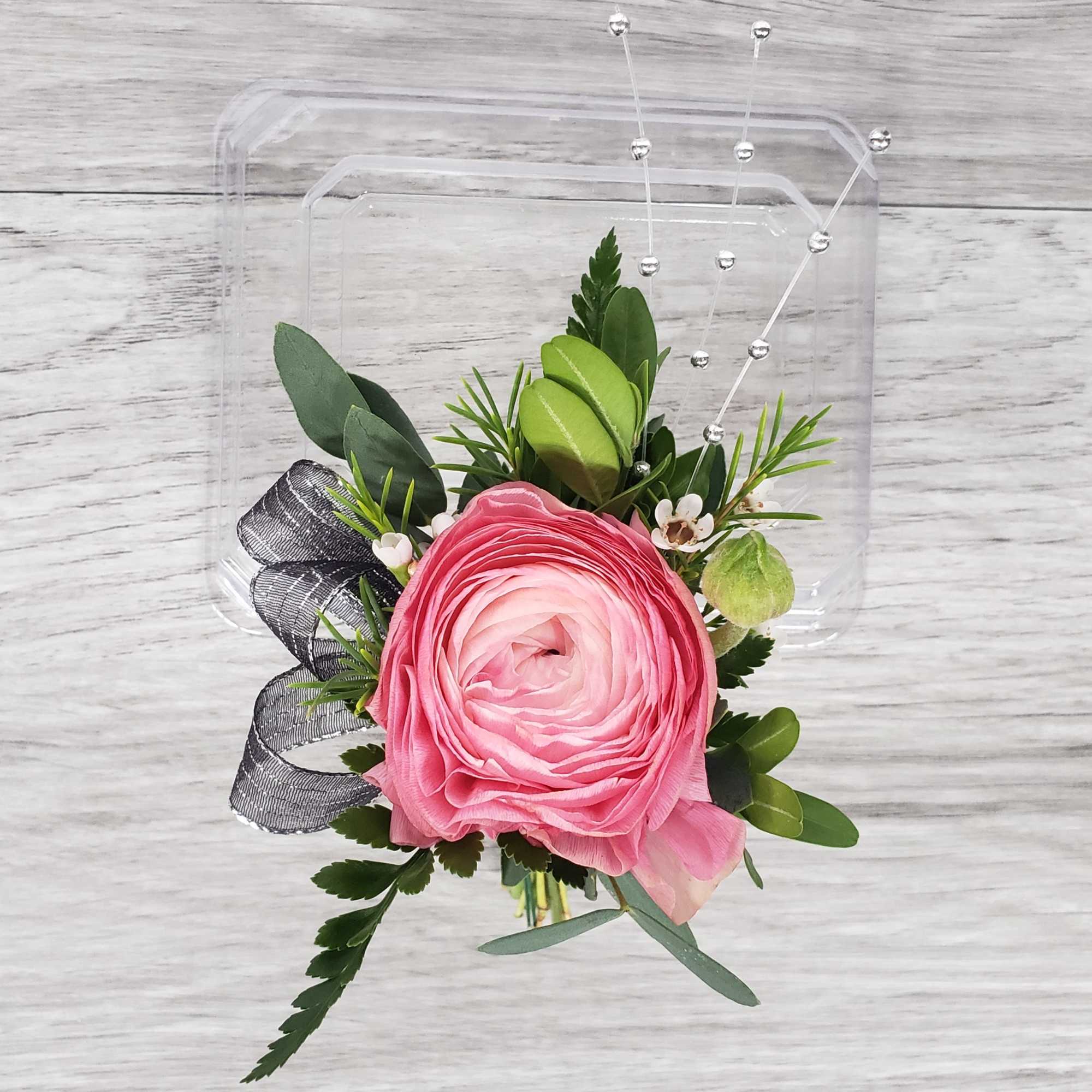 Pink ranunculus boutonniere with greenery and black ribbon