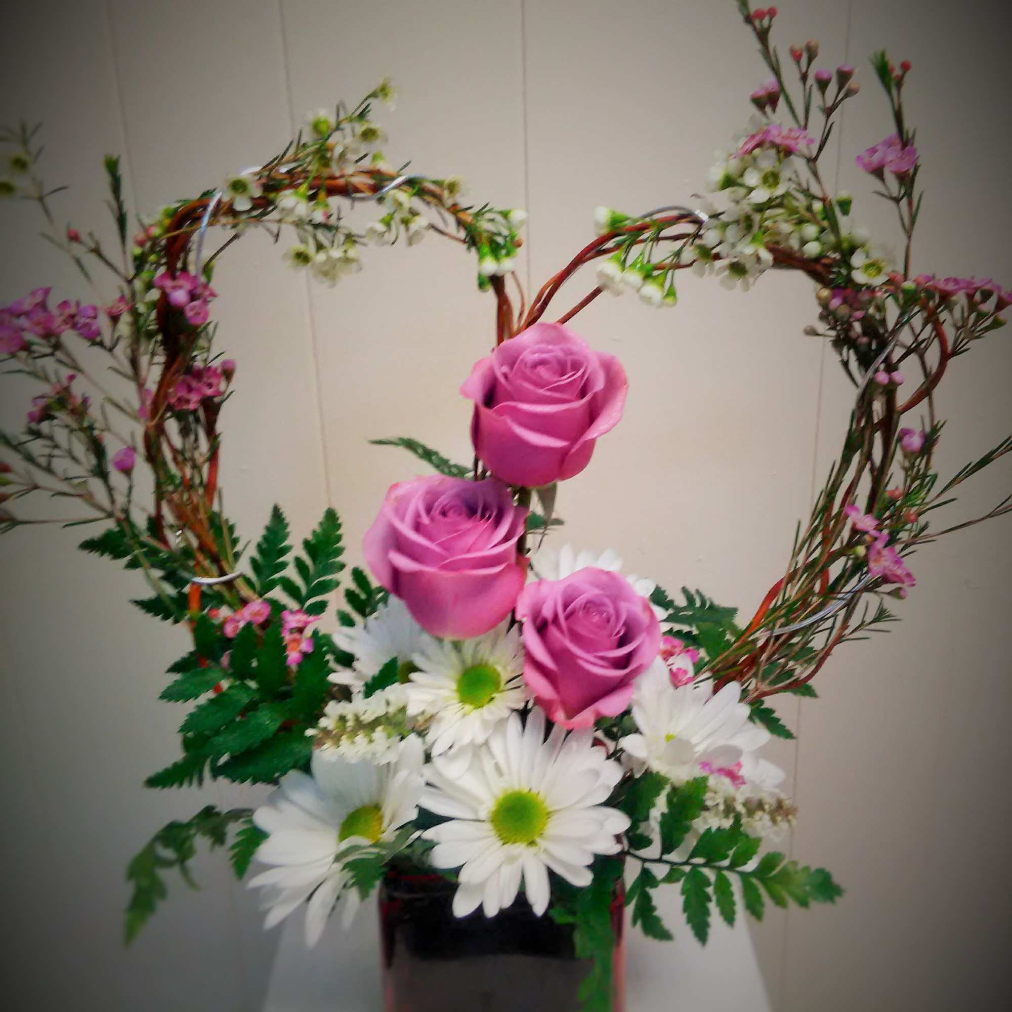 Pink roses and white daisies in a square vase with heart-shaped branches