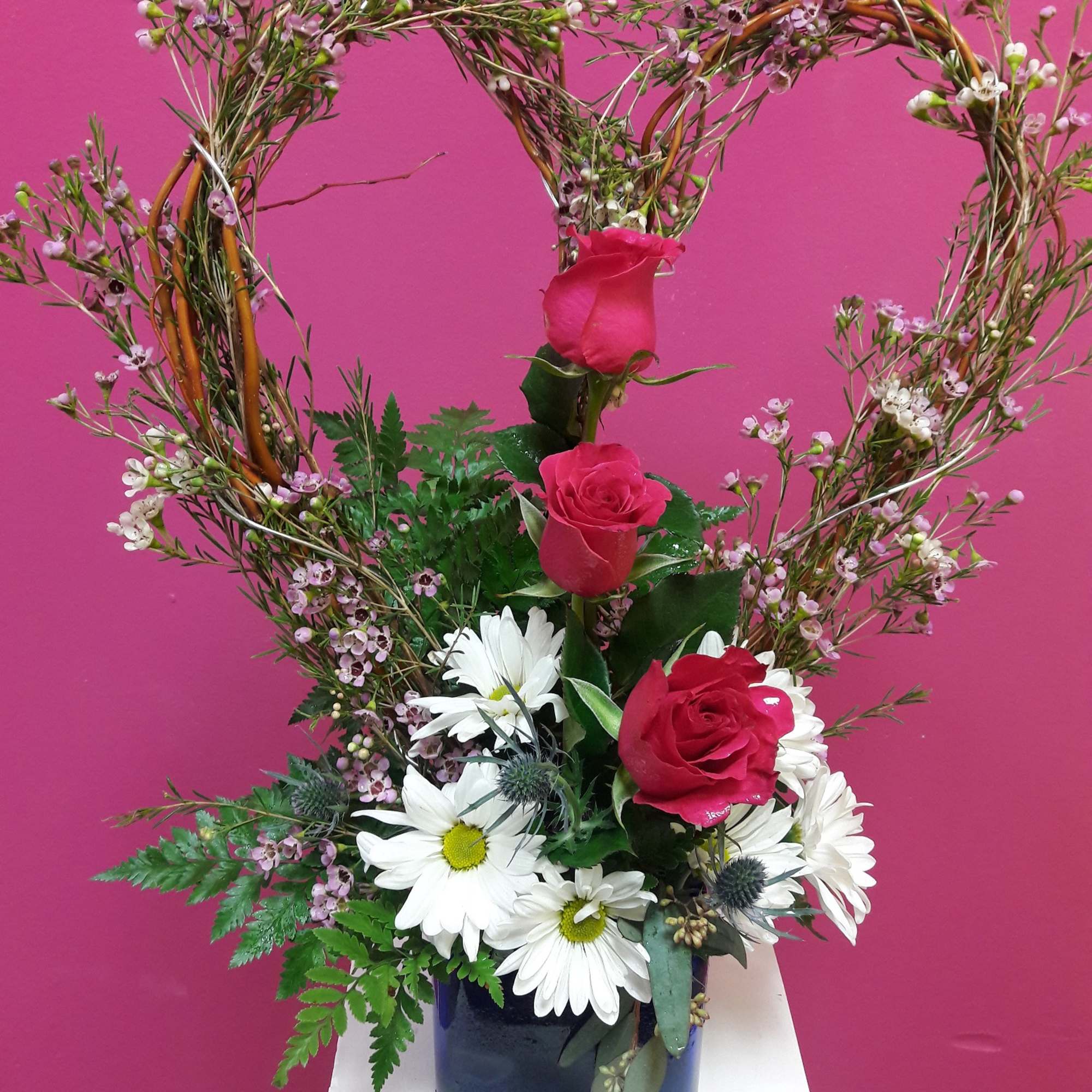 Heart-shaped floral arrangement with red roses and white daisies in a dark vase
