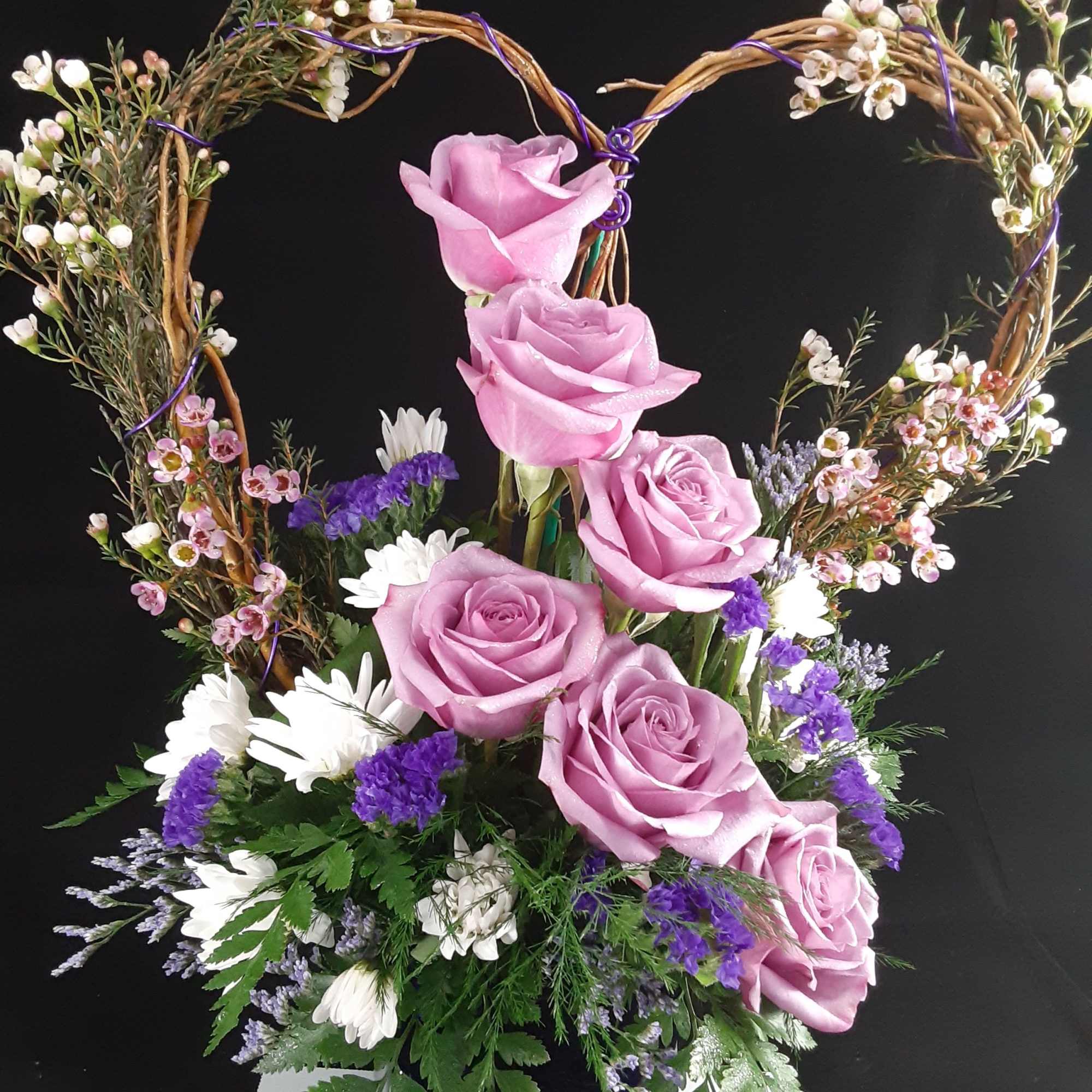 Pink roses in a heart-shaped floral arrangement with white and purple accents