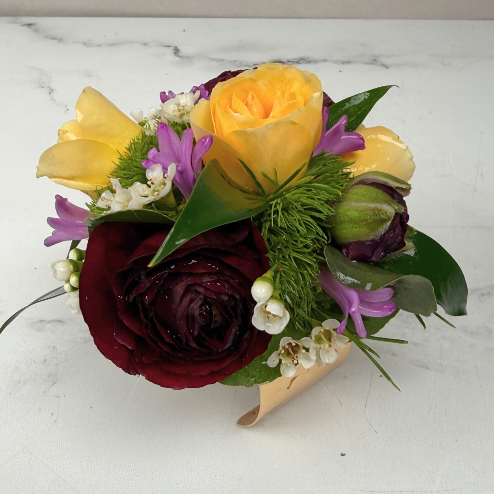 A lush burgundy ranunculus takes center stage in this Velvet Meadow Corsage