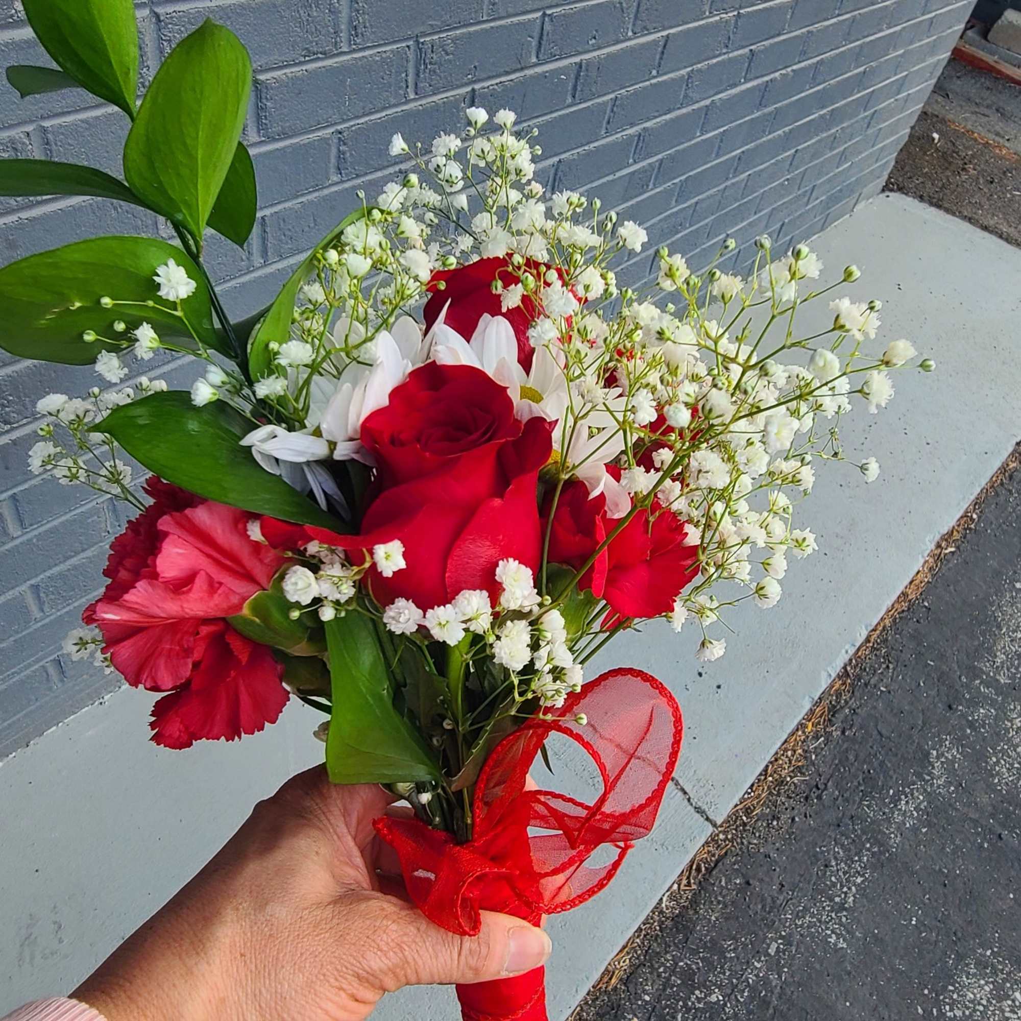 Vivid red roses take center stage in this handheld flower arrangement, making