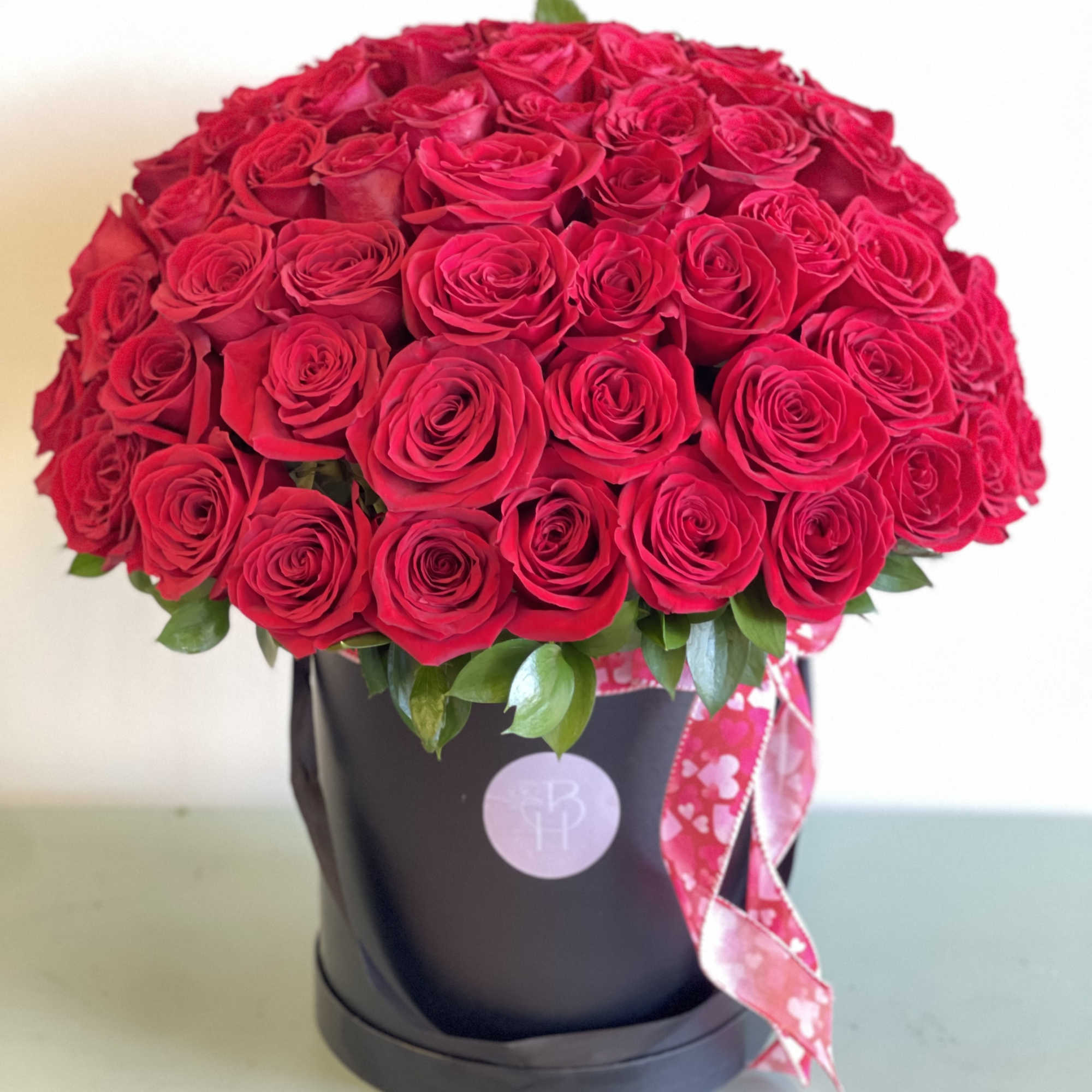 Large bouquet of red roses in a black hatbox with a pink ribbon