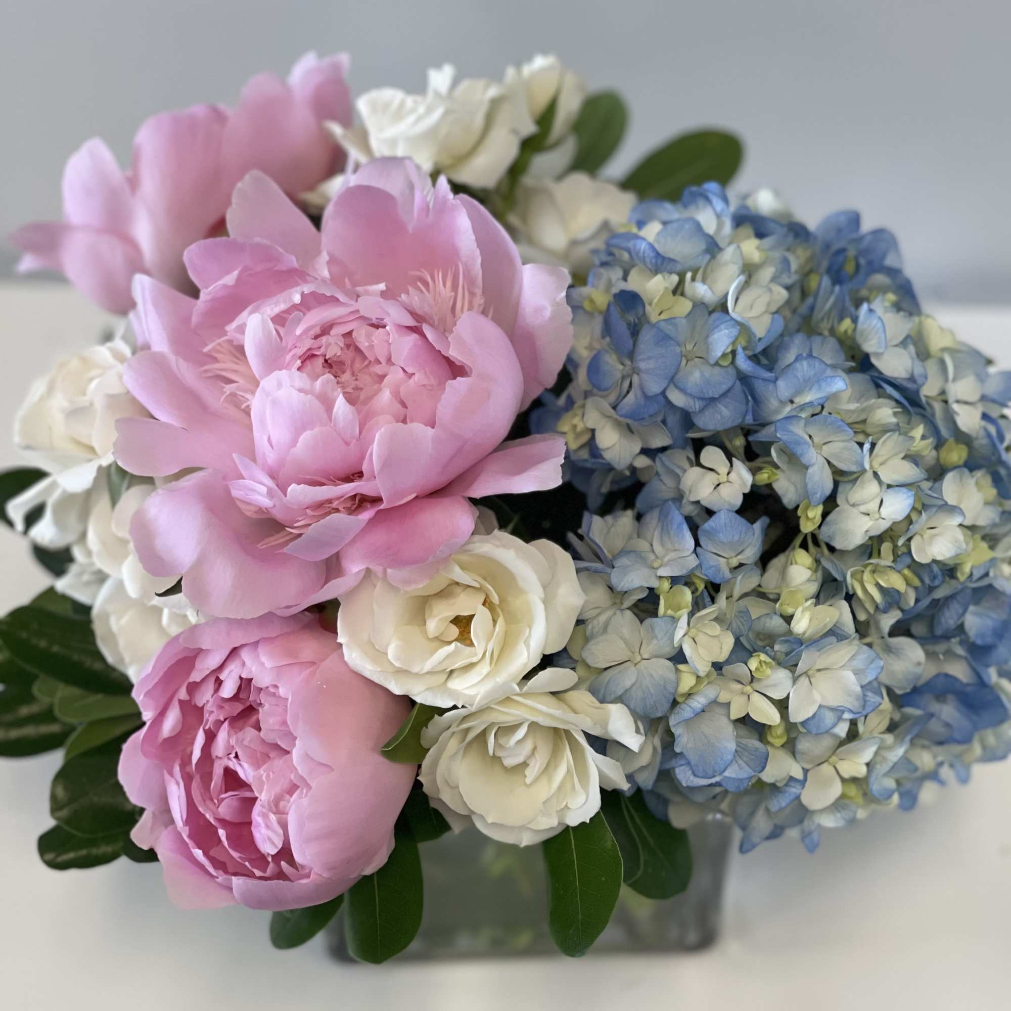 Pink peonies, white roses, and blue hydrangeas in a square vase