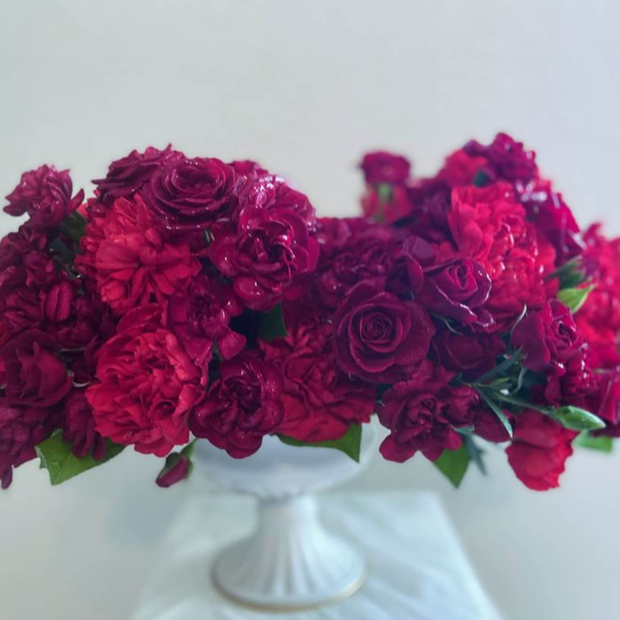 Deep pink and burgundy flower arrangement in a white pedestal vase