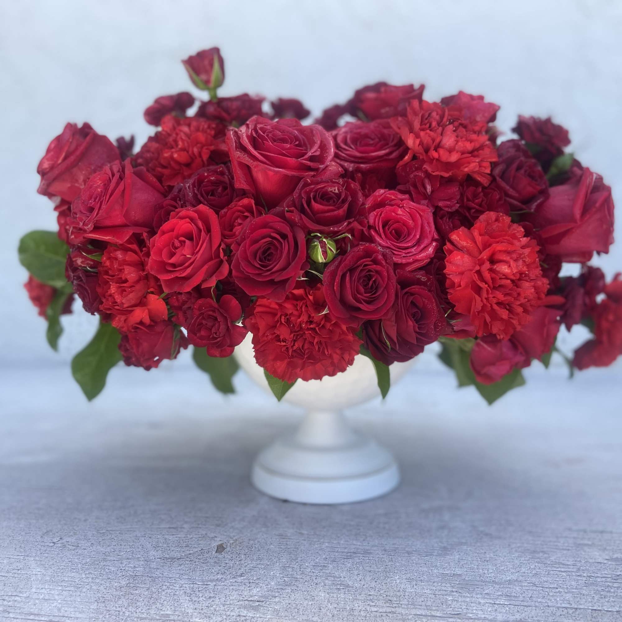 Red rose and carnation arrangement in a white pedestal vase