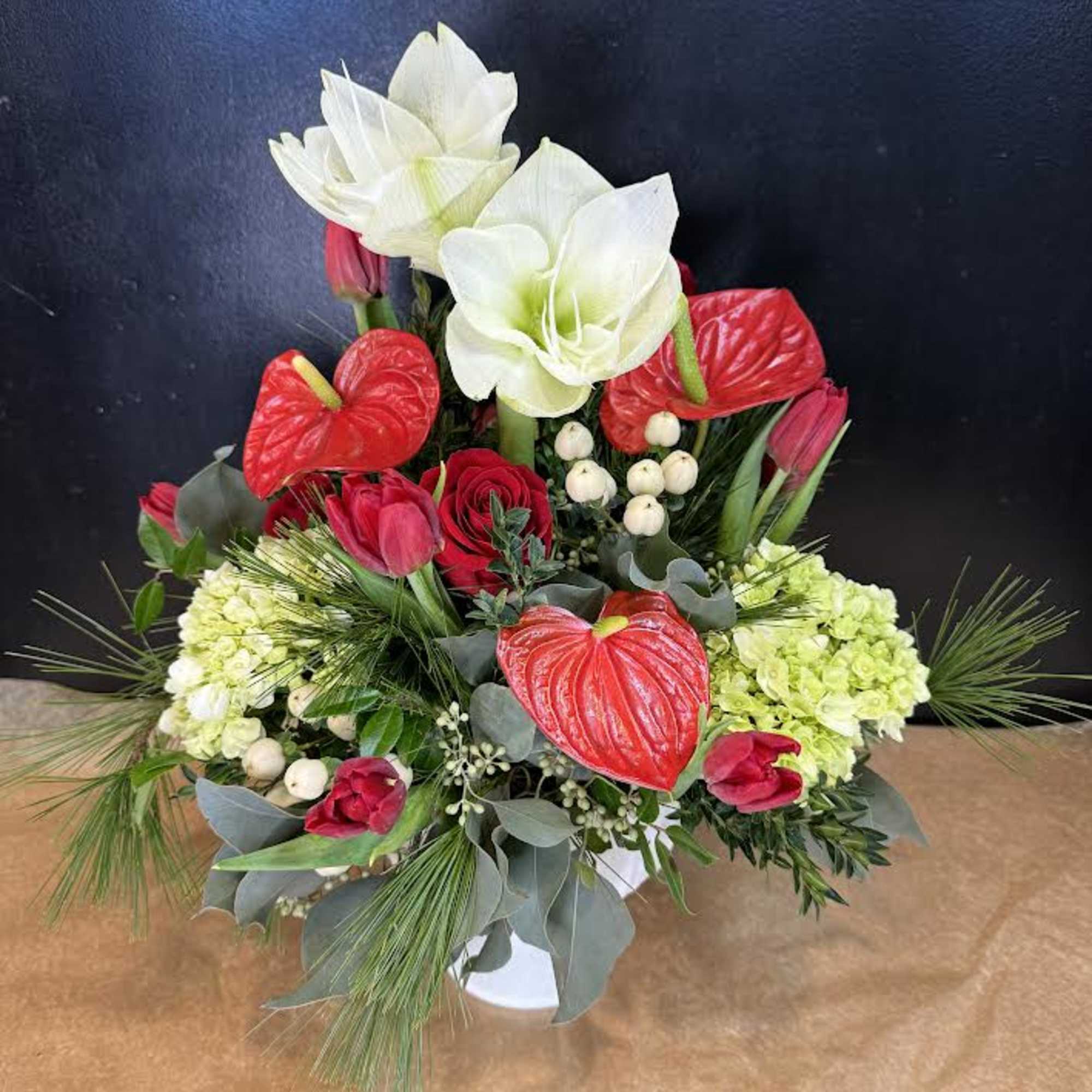Red and white floral arrangement with tulips, anthuriums, and lilies in a white vase