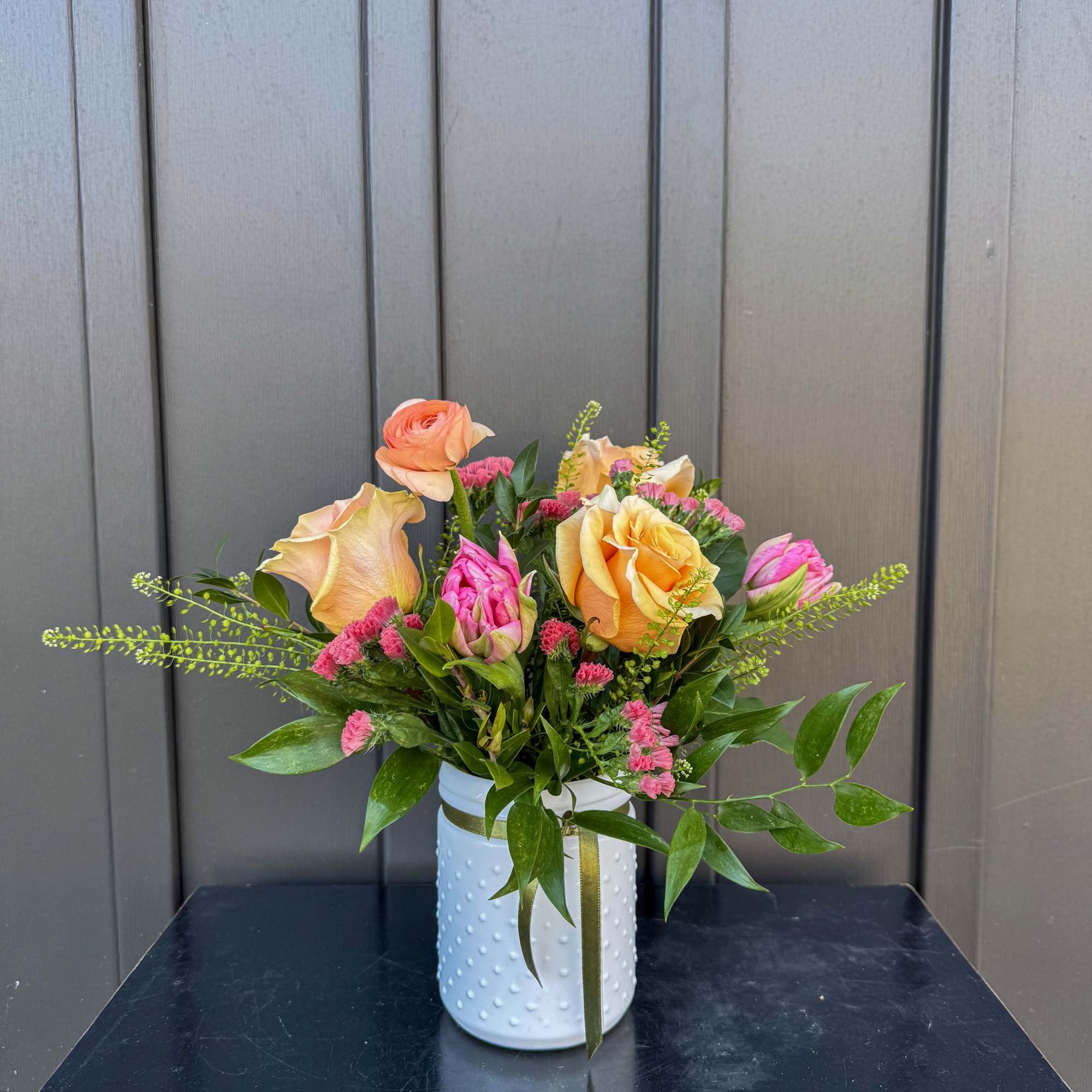Peach and pink roses with small pink blooms in a white textured vase