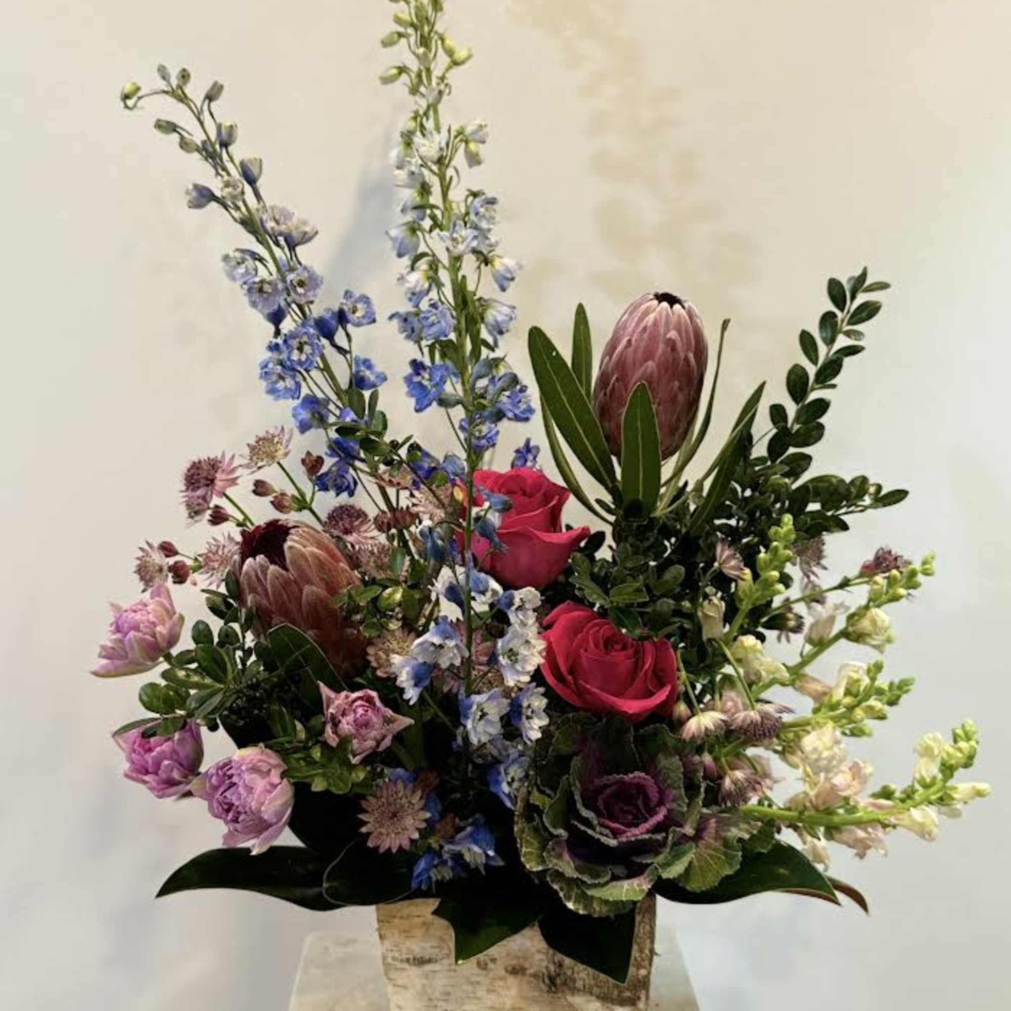 Mixed floral arrangement in a rustic square vase with pink and blue blooms