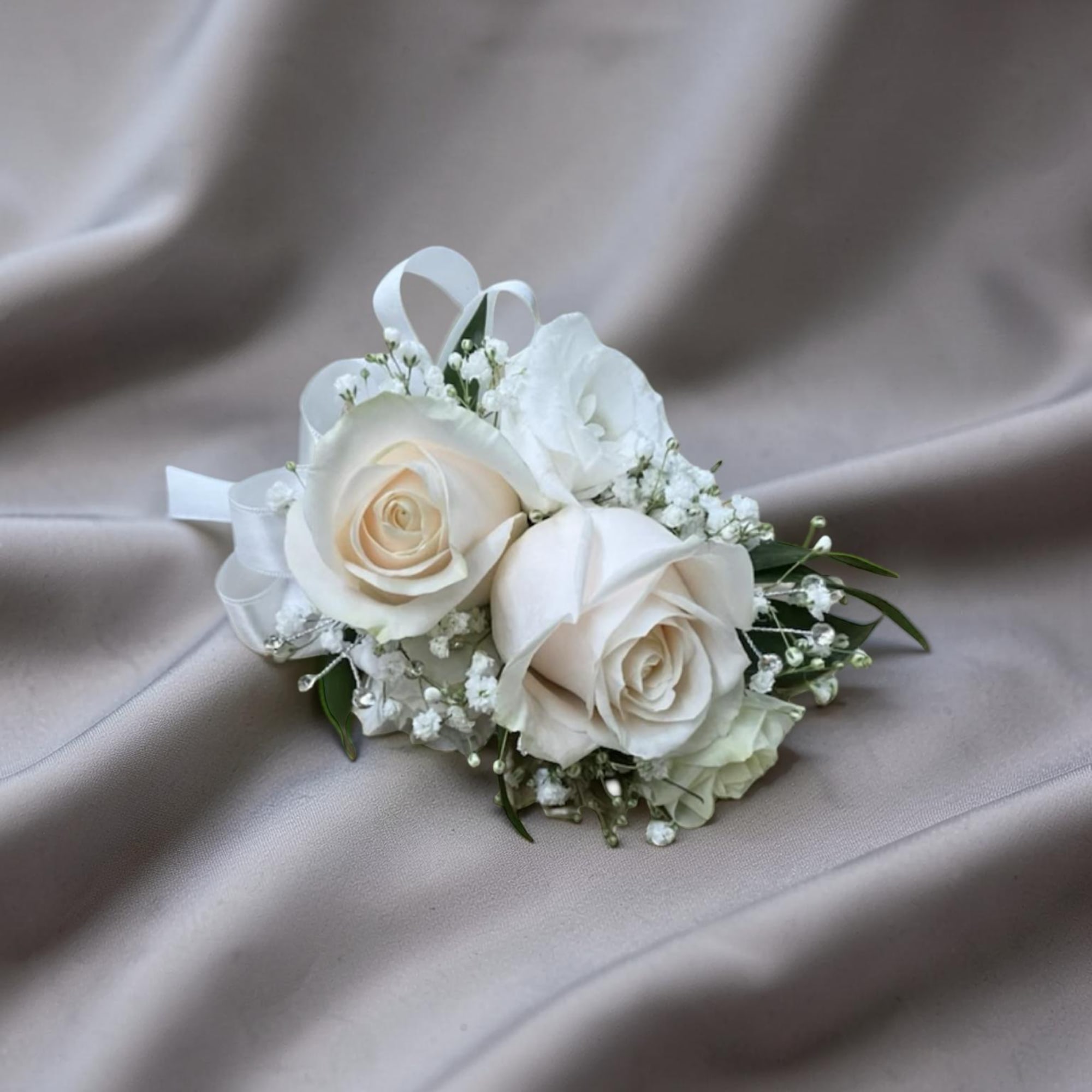 A soft and elegant corsage featuring ivory roses, delicate baby&rsquo;s breath, and