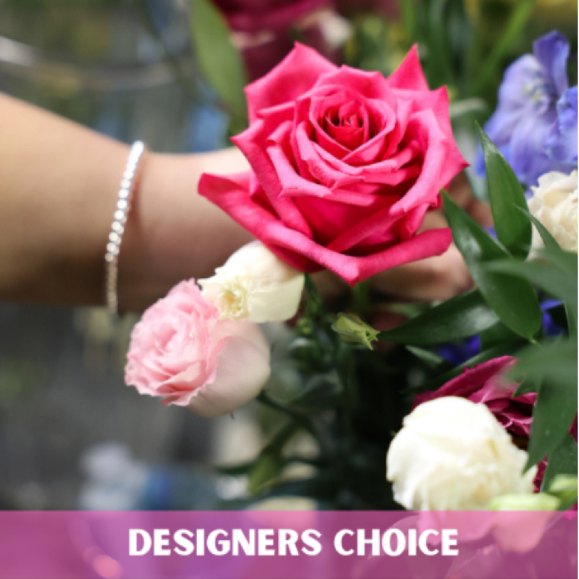 Florist hand holding a bright pink rose with small white and blush roses, labeled designers choice