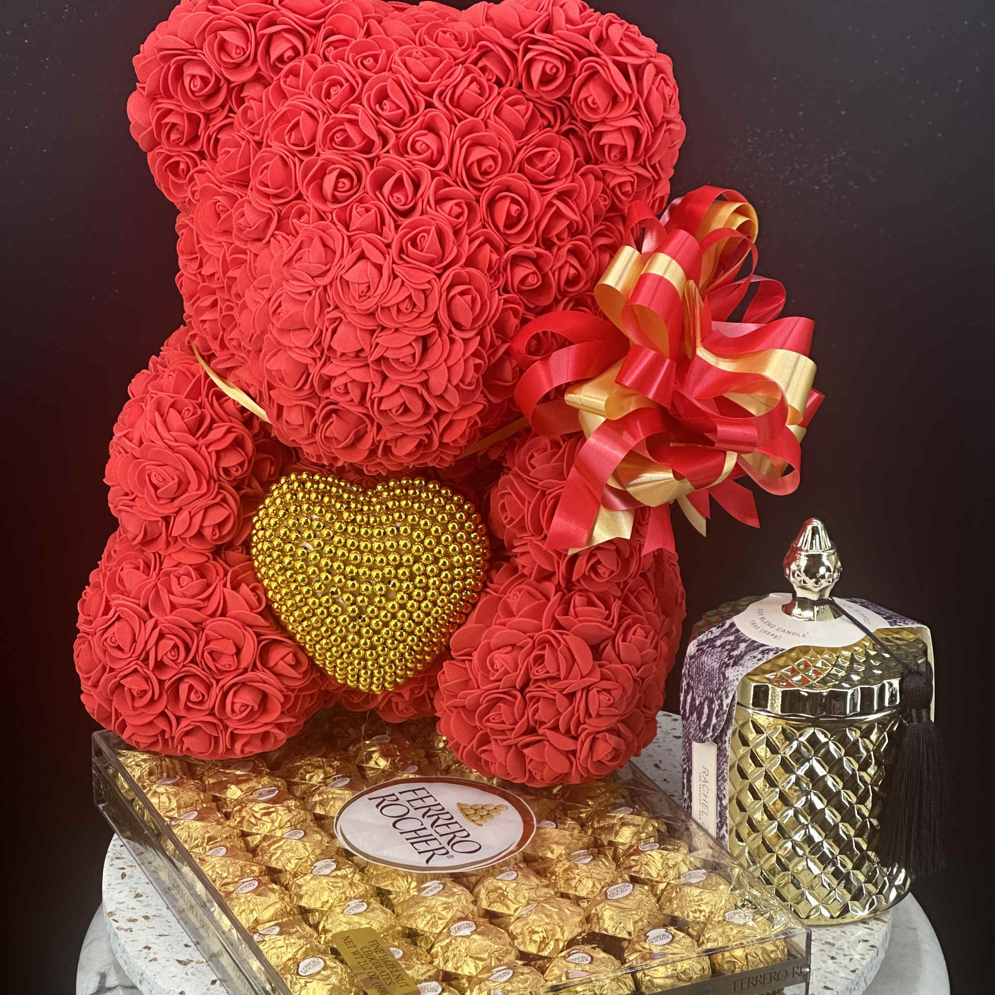Red rose teddy bear with a gold heart and gift ribbon beside chocolates