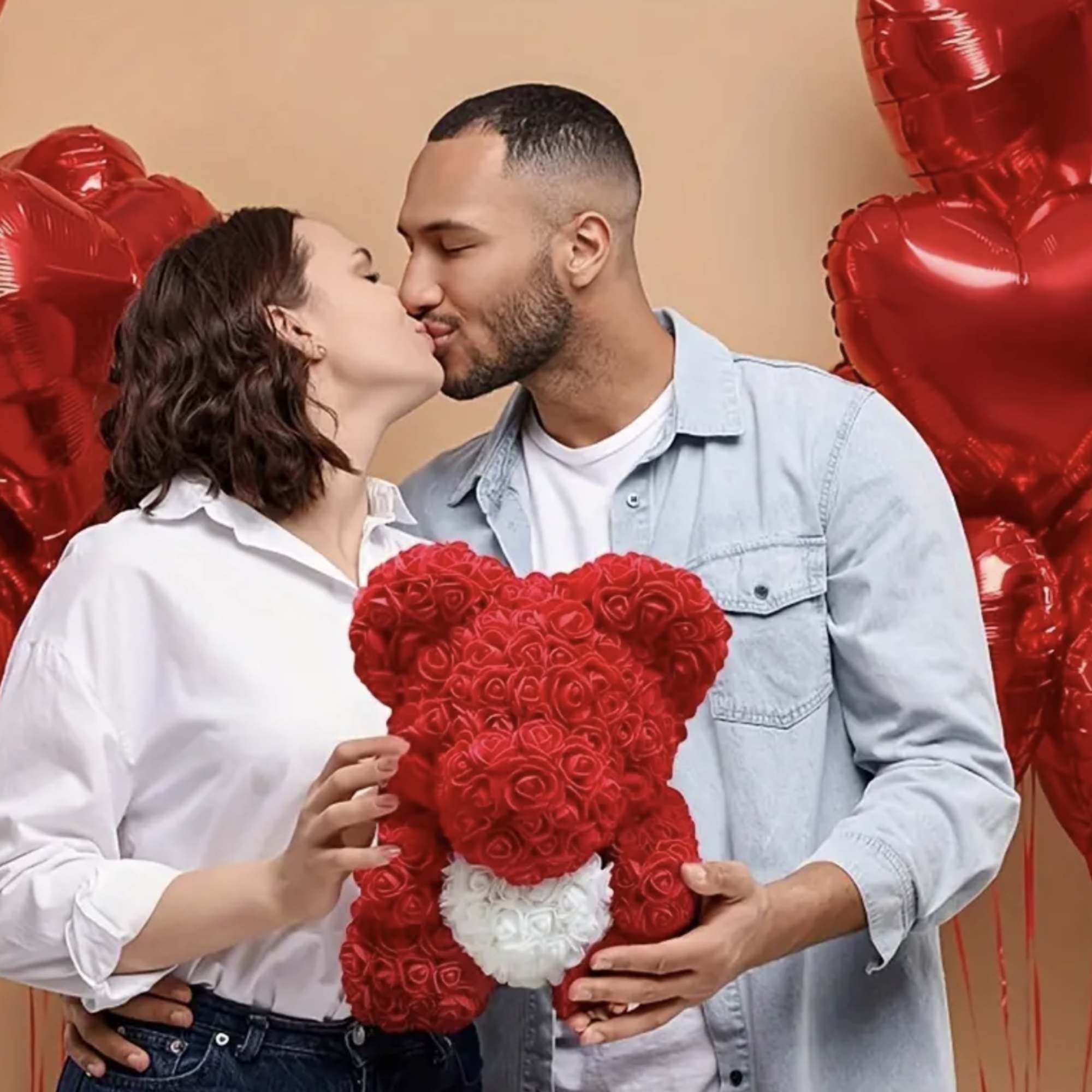 Couple kissing while holding a red rose teddy bear with heart balloons behind them