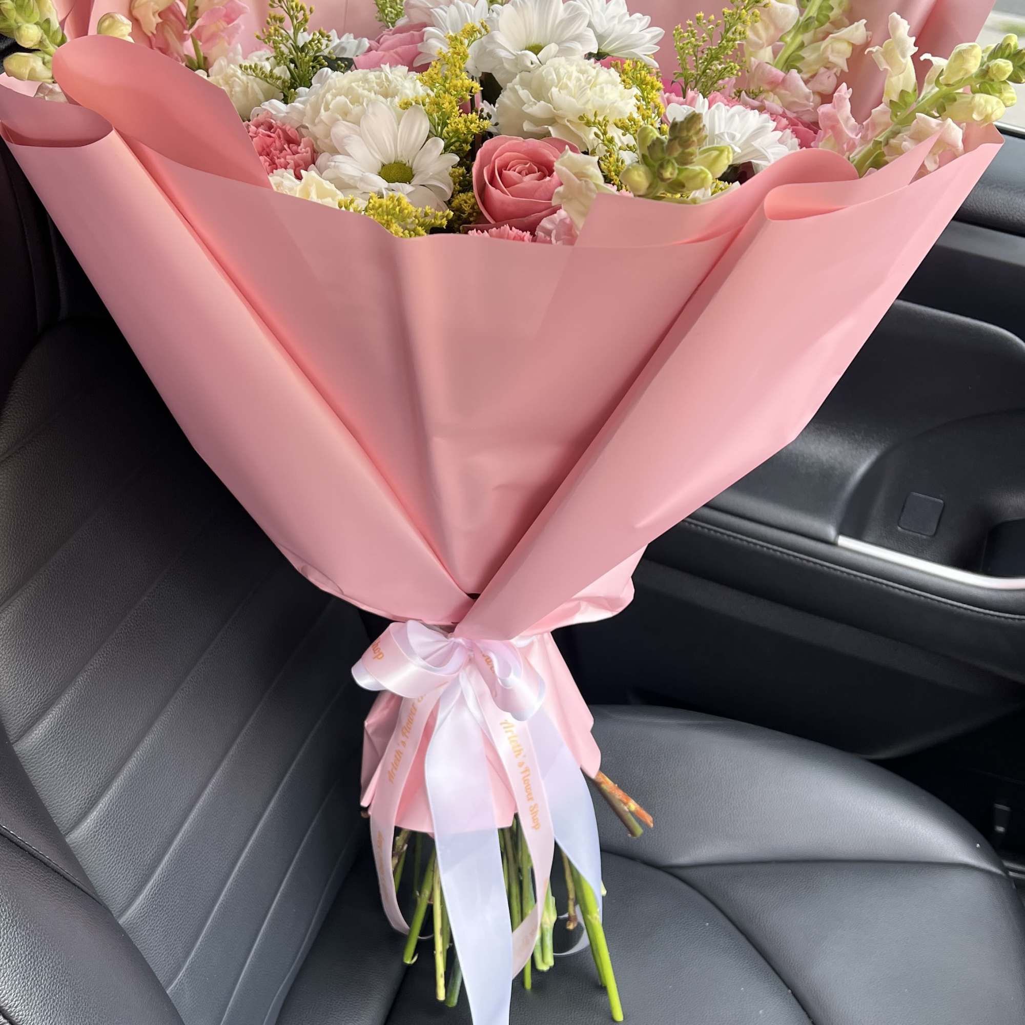 Pink-wrapped bouquet with white daisies, pink roses, and snapdragons