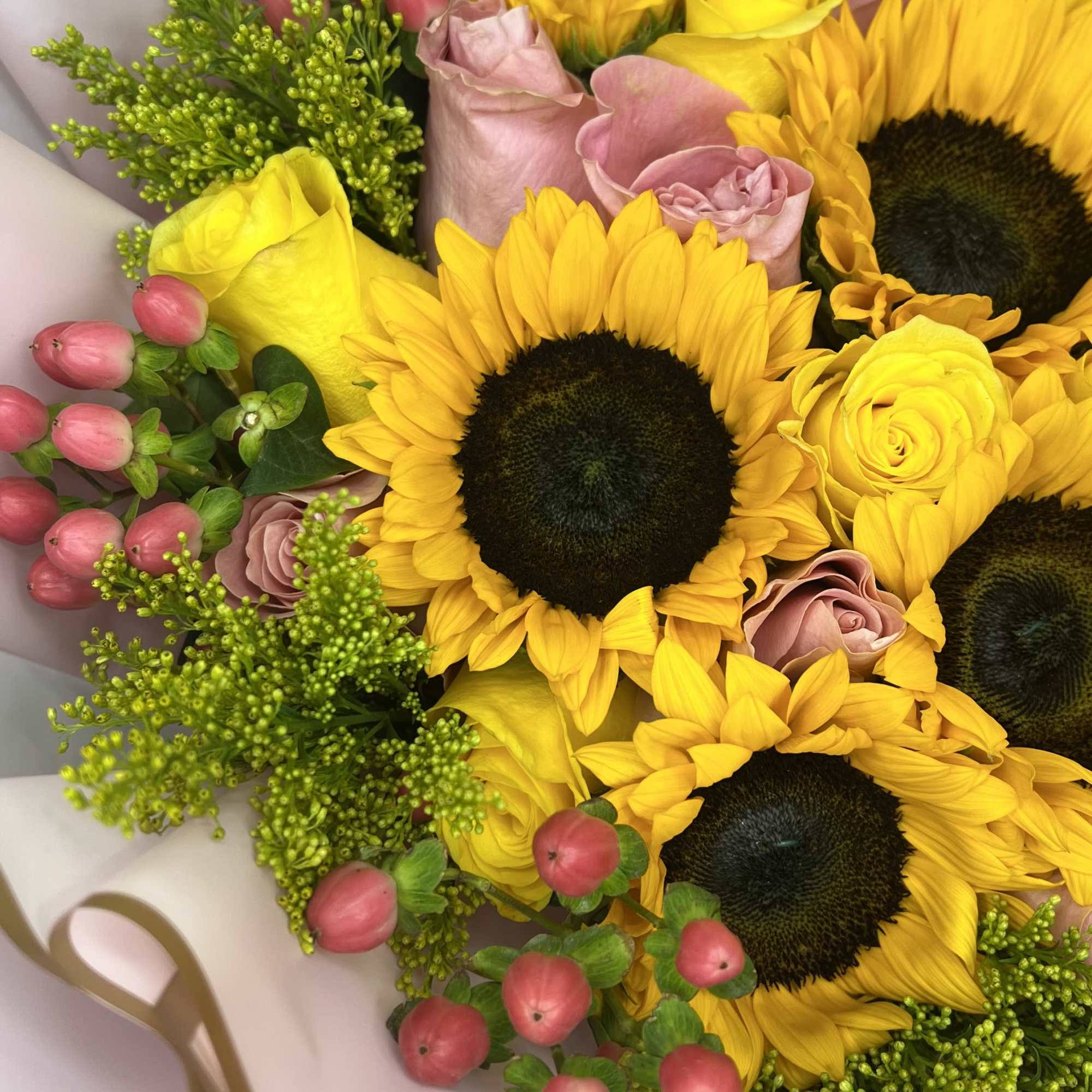Bouquet of sunflowers, yellow roses, and pink buds wrapped in pale paper