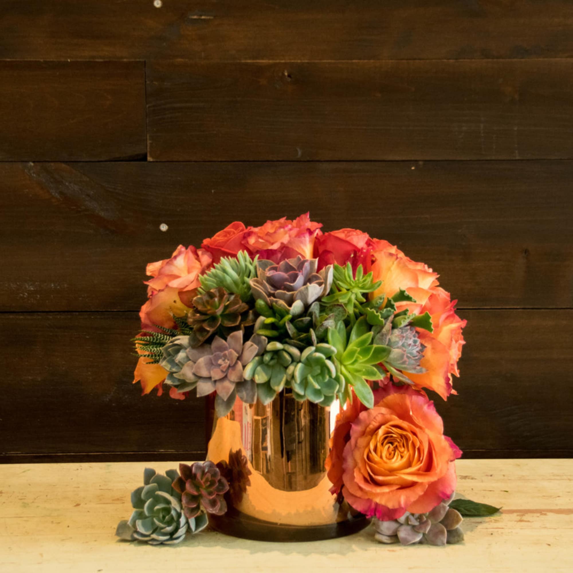 Succulent arrangement with orange roses in a gold vase
