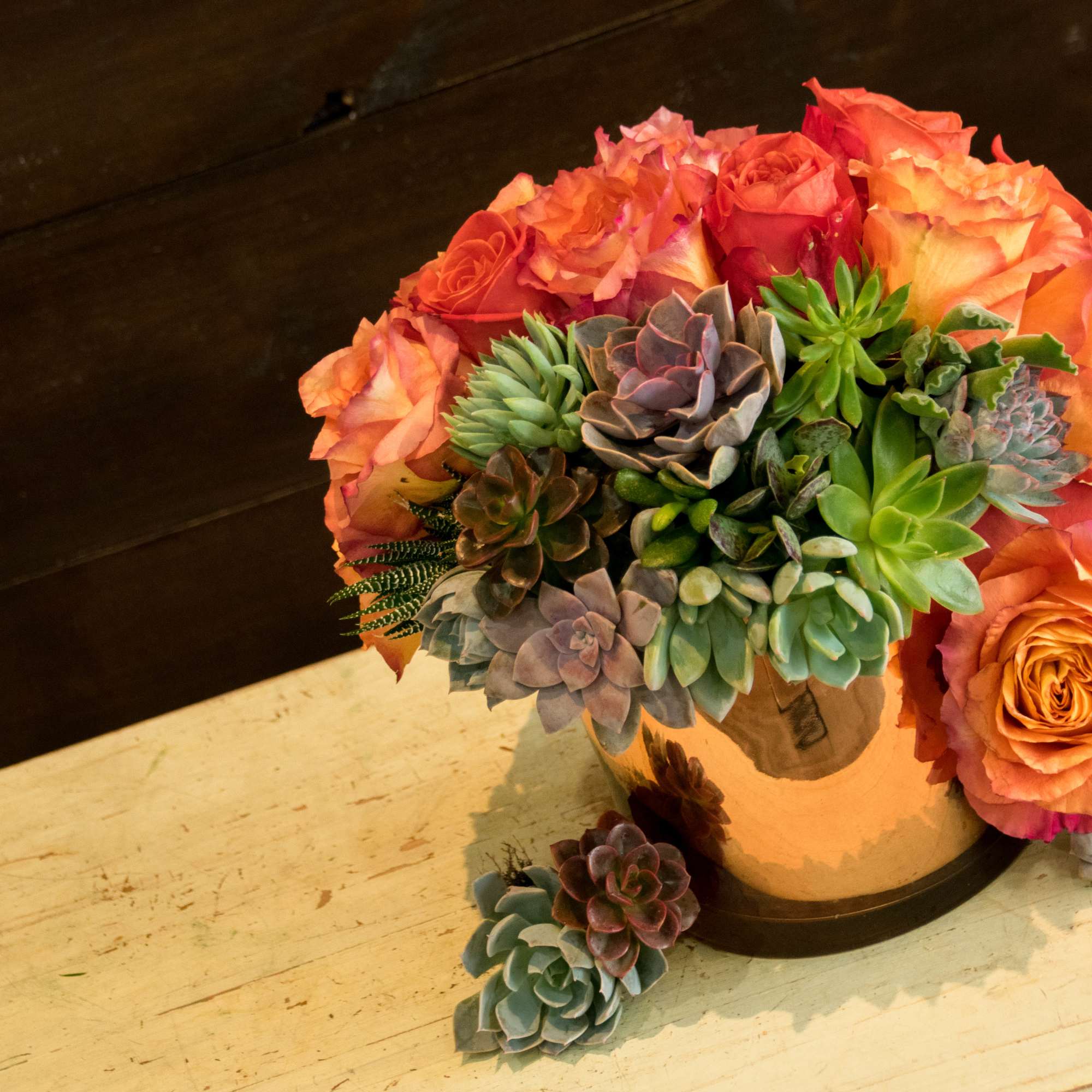 Orange roses and succulents arranged in a small pot