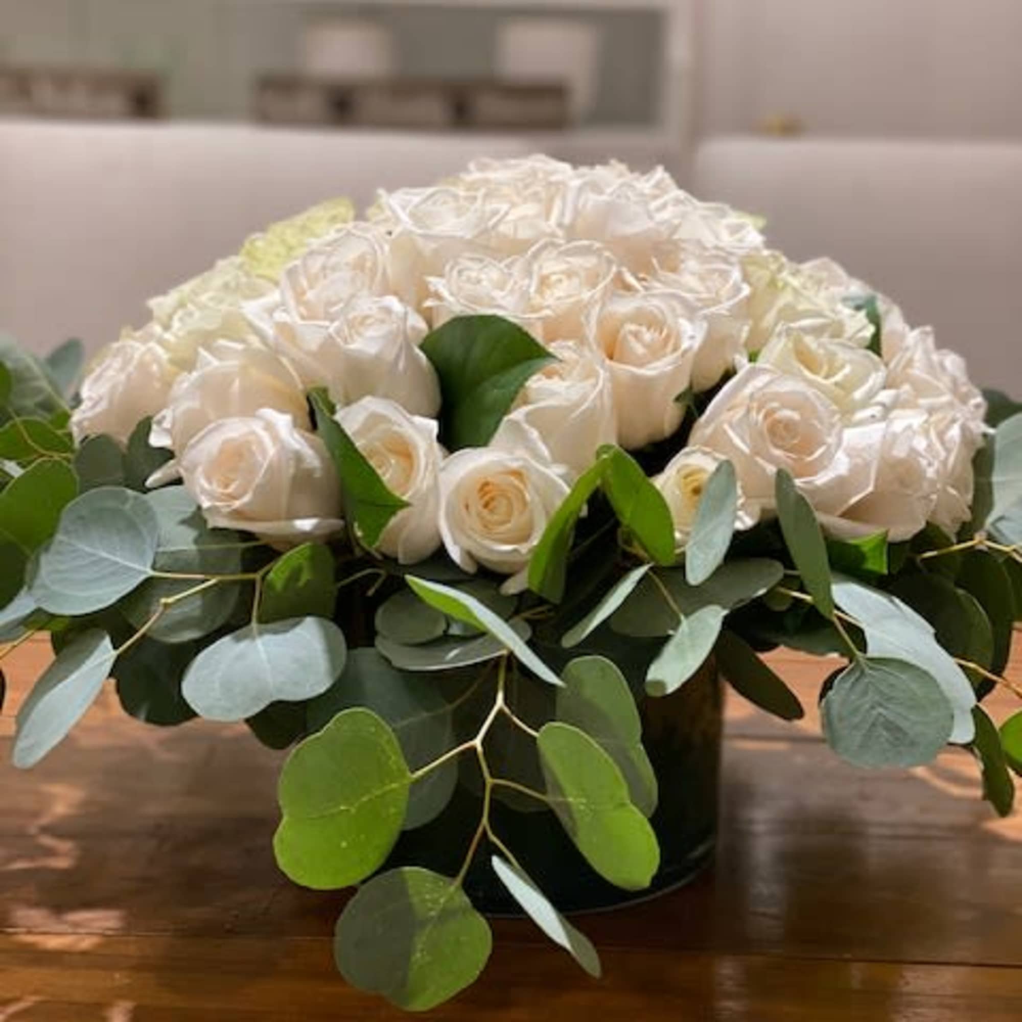 Low arrangement of ivory roses in a round vase with a collar of eucalyptus.