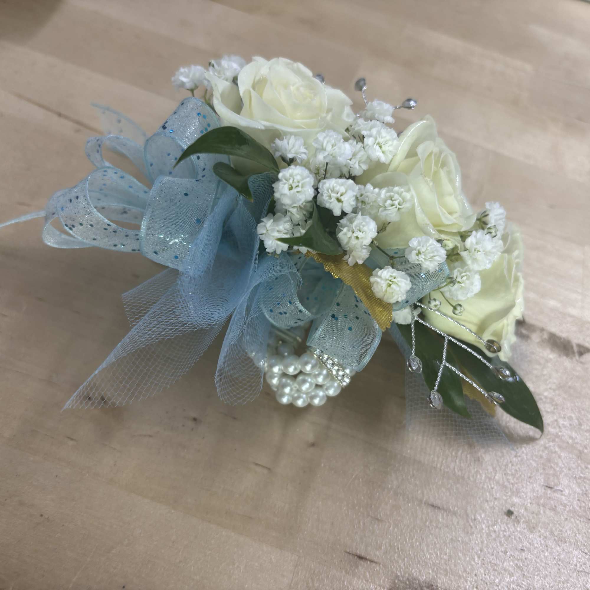 This classic wrist corsage features soft white roses, delicate baby&rsquo;s breath, and