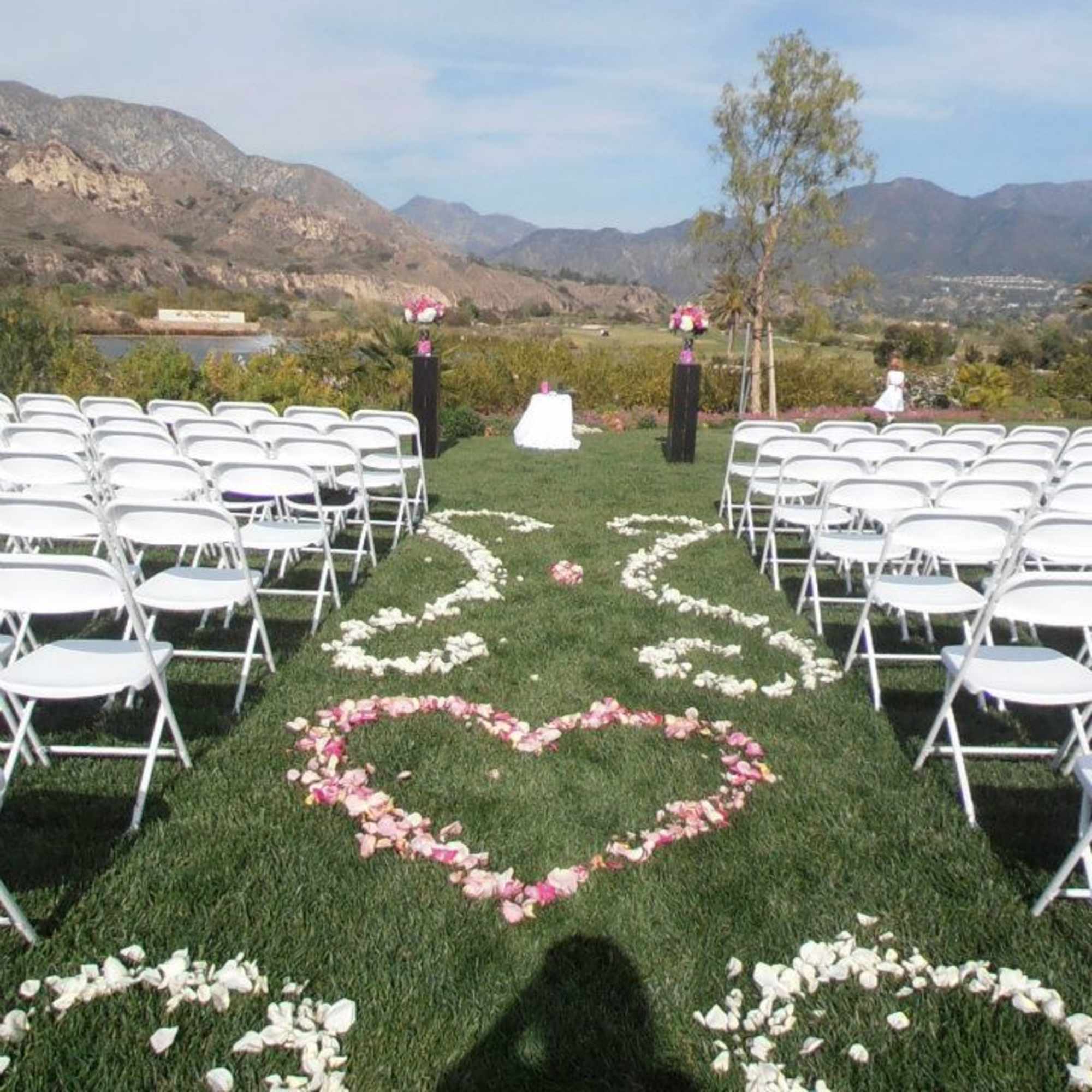 Outdoor wedding aisle with white chairs and flower petal heart designs on grass
