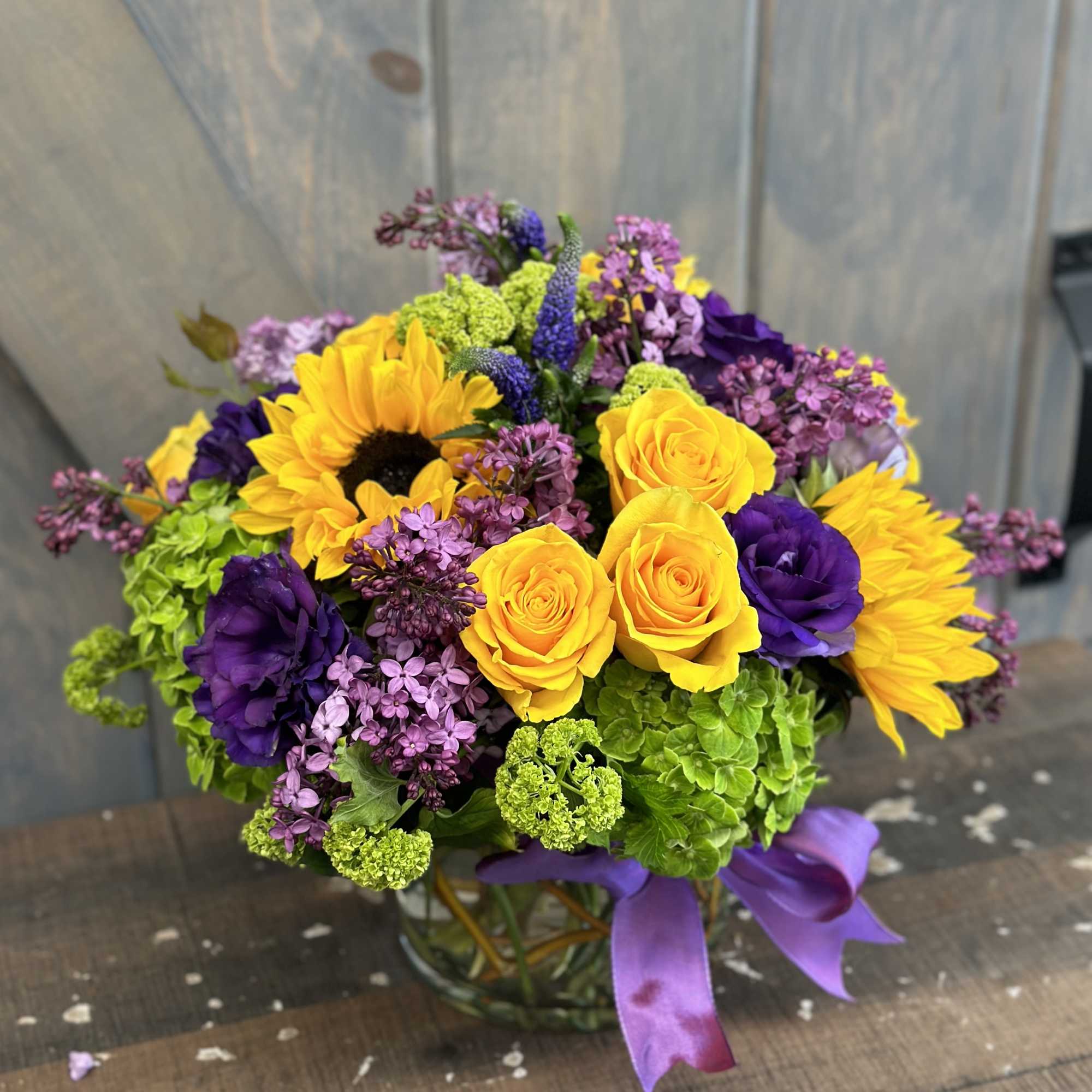 Bright bouquet of yellow roses, sunflowers, and purple flowers in a glass vase