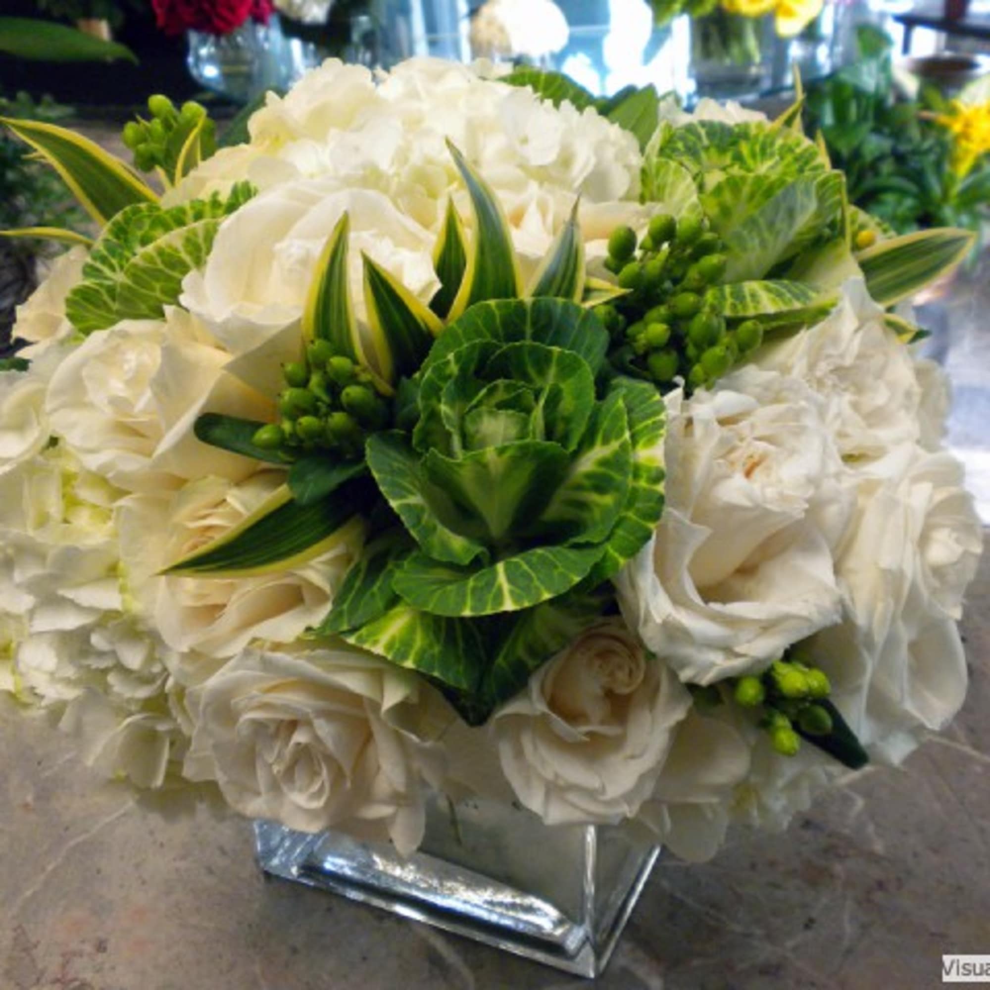 White rose bouquet with green variegated foliage in a square vase