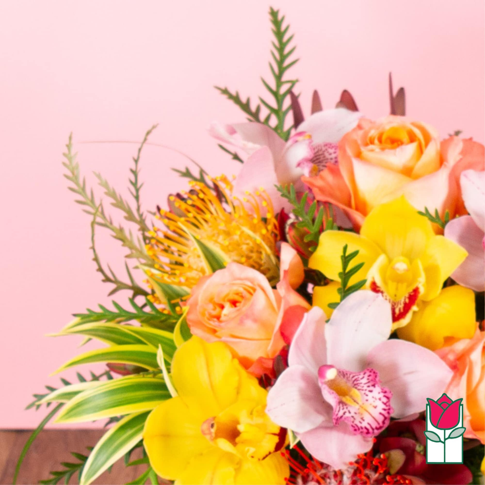 Bright bouquet of yellow orchids, peach roses, and pink orchids against a soft pink background