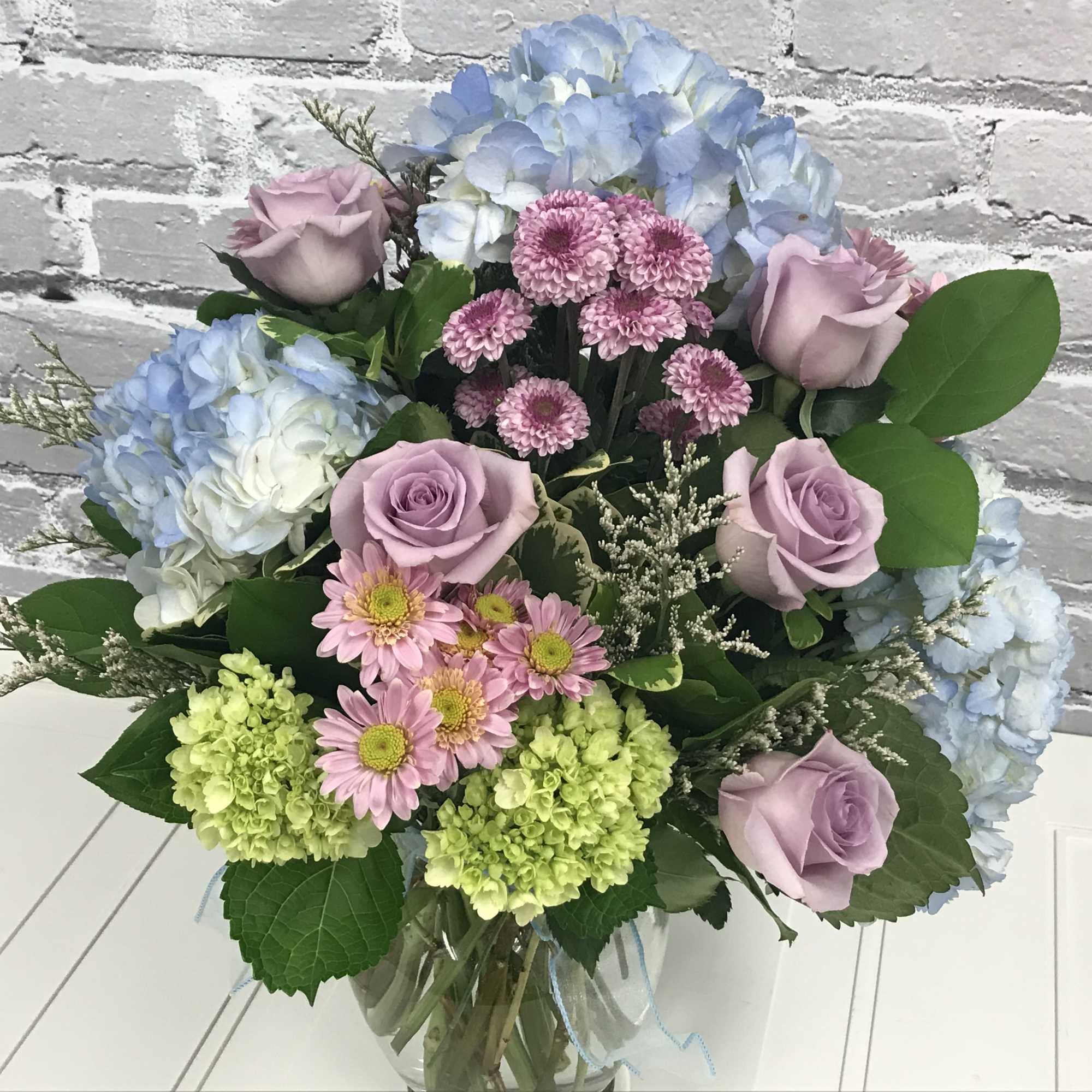 Bouquet of lavender roses, blue hydrangeas, and pink daisies in a glass vase