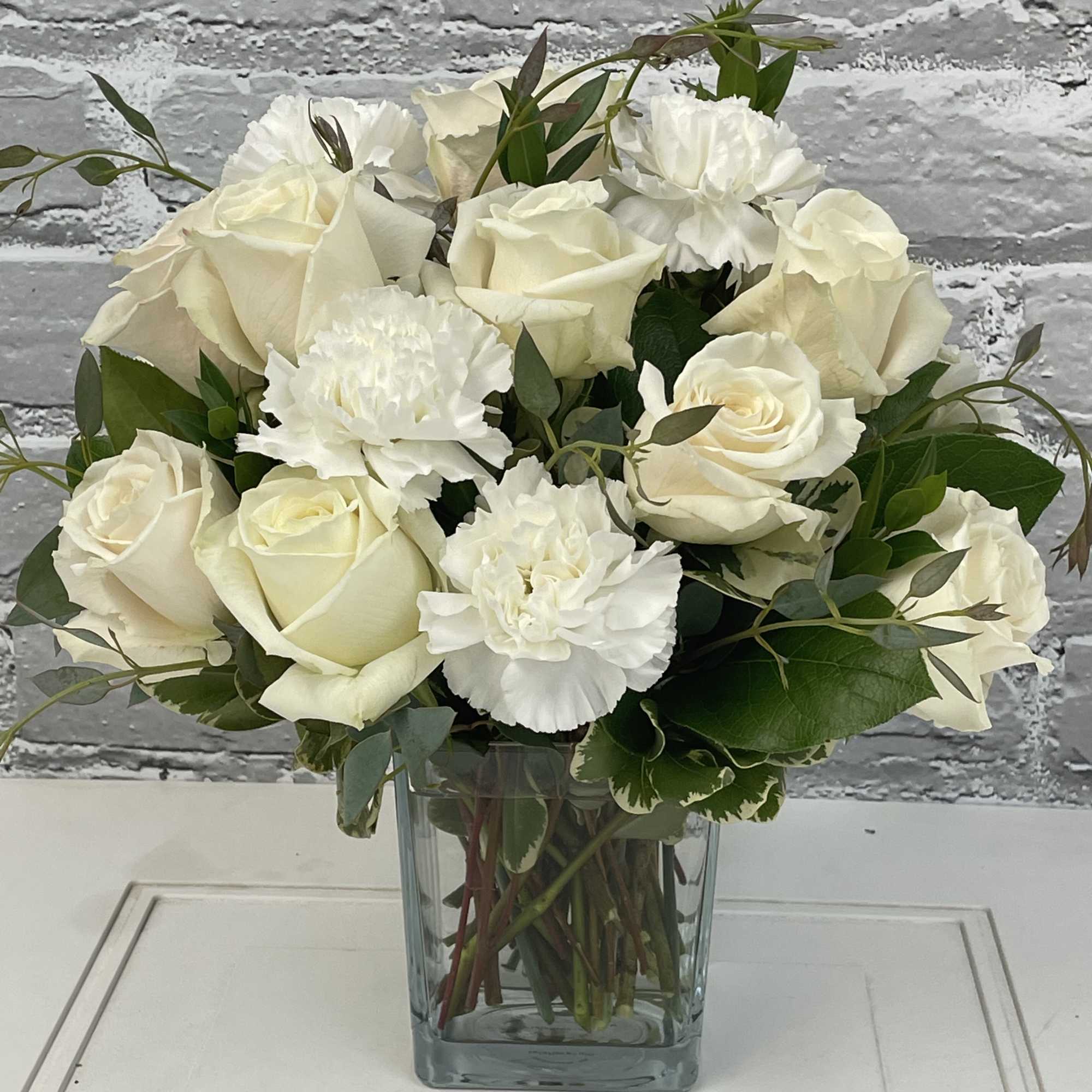 White roses and carnations arranged in a clear glass vase