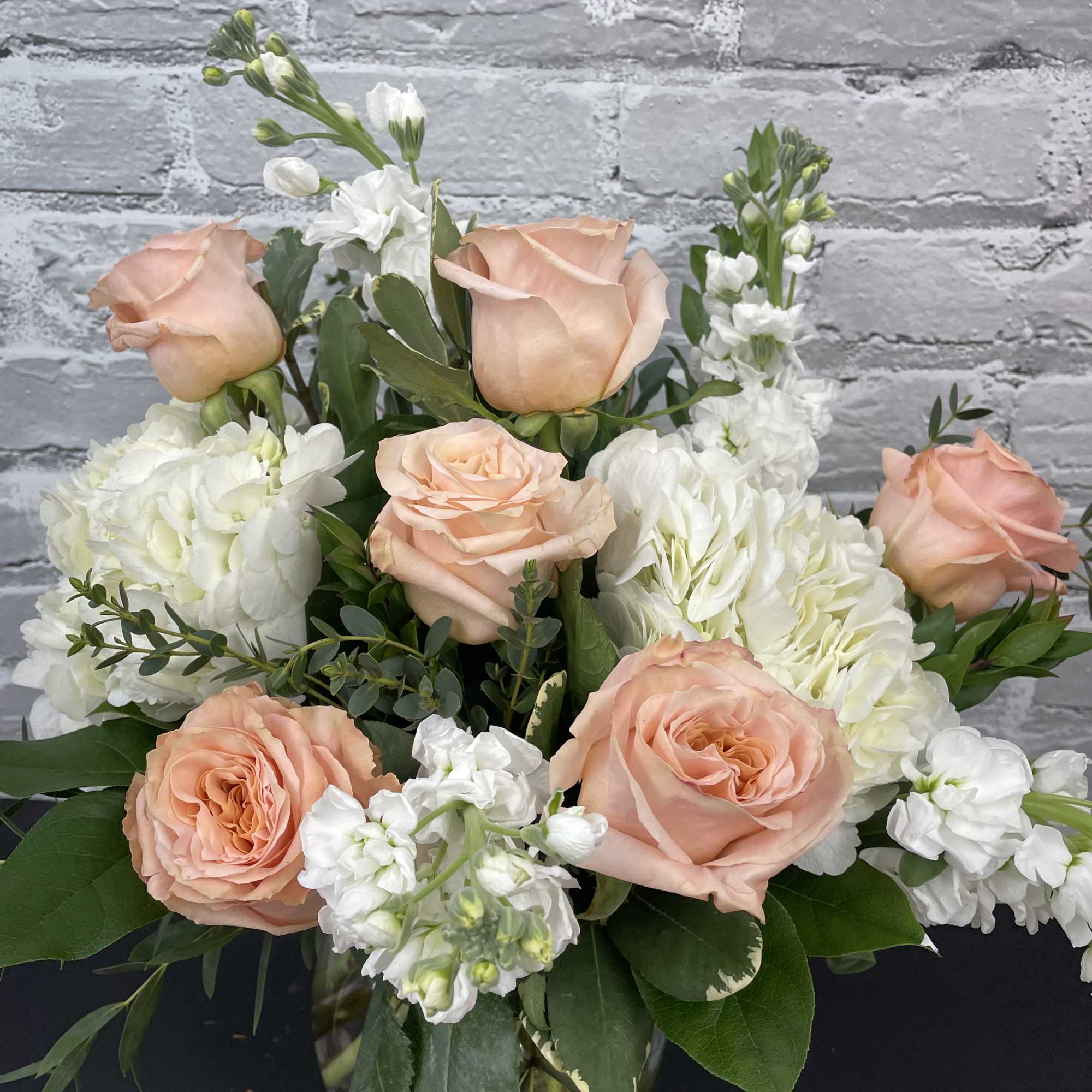 Peach roses and white flowers arranged in a glass vase