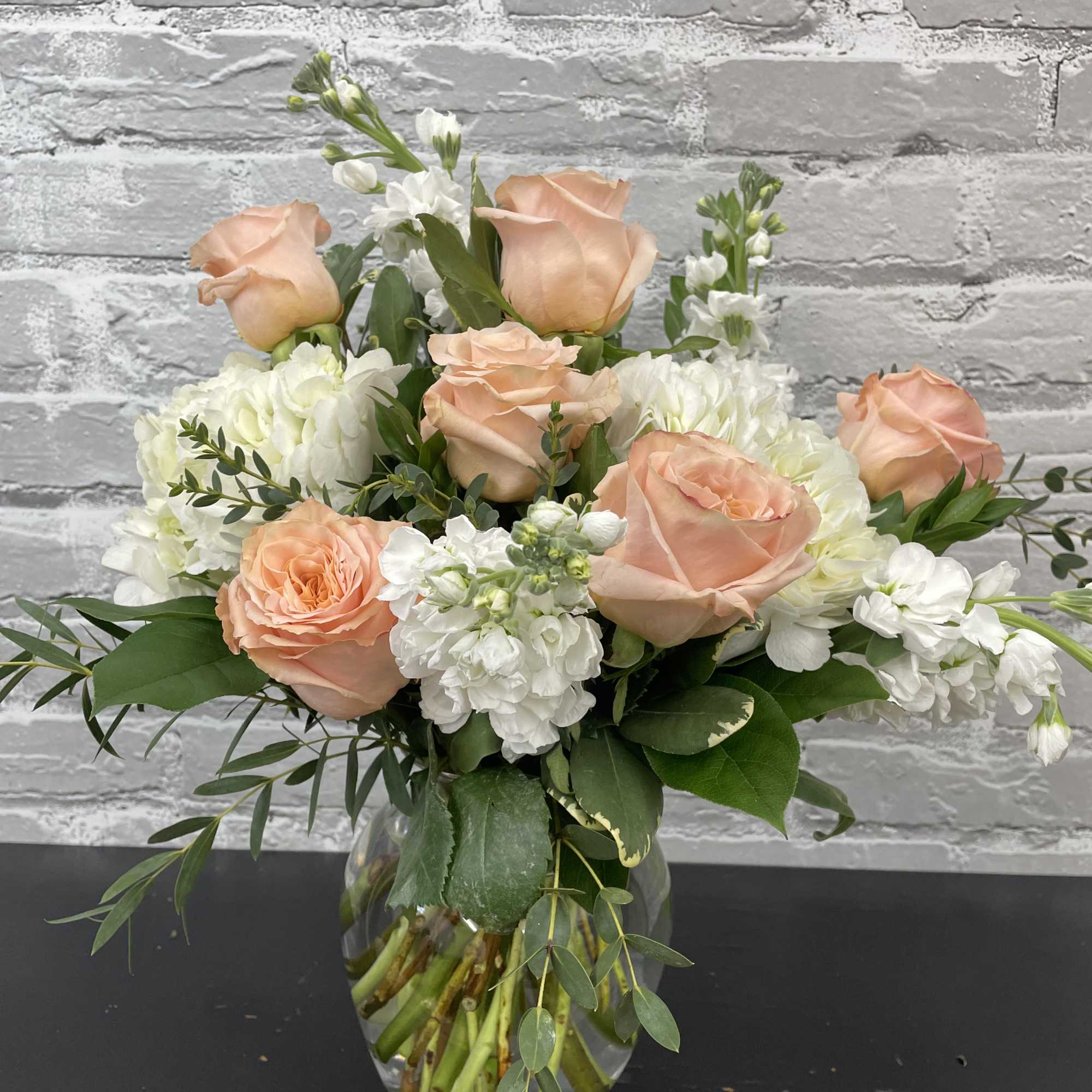 Peach roses and white flowers arranged in a clear glass vase