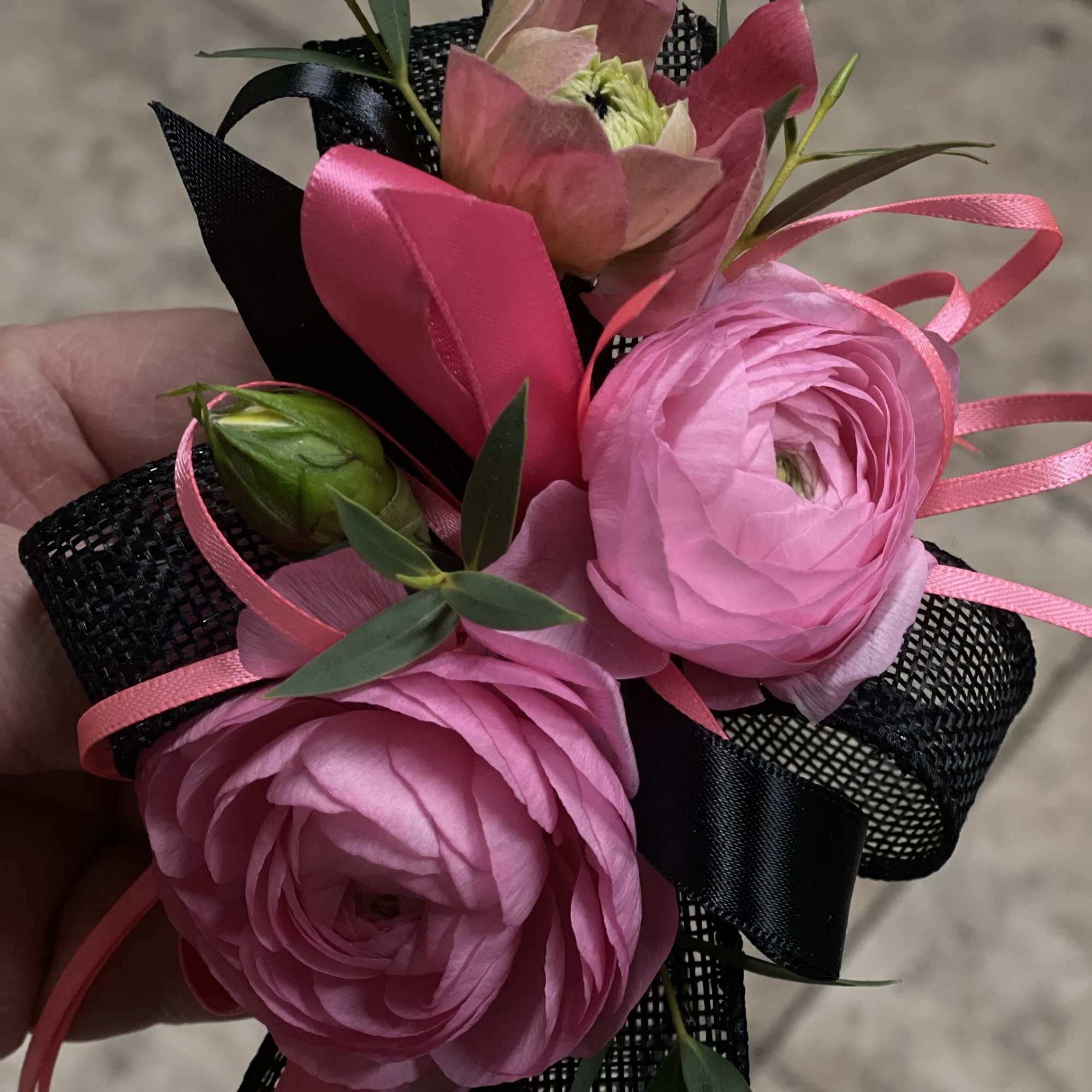 A bold and stylish wrist corsage featuring vibrant pink ranunculus, delicate accent