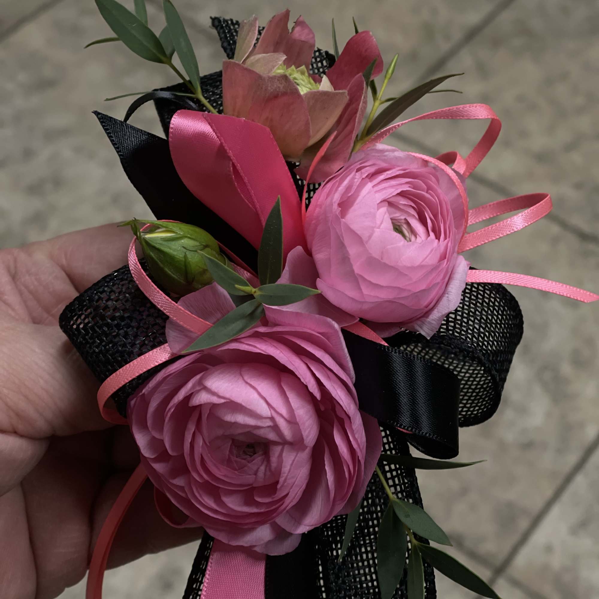 A bold and stylish wrist corsage featuring vibrant pink ranunculus, delicate accent