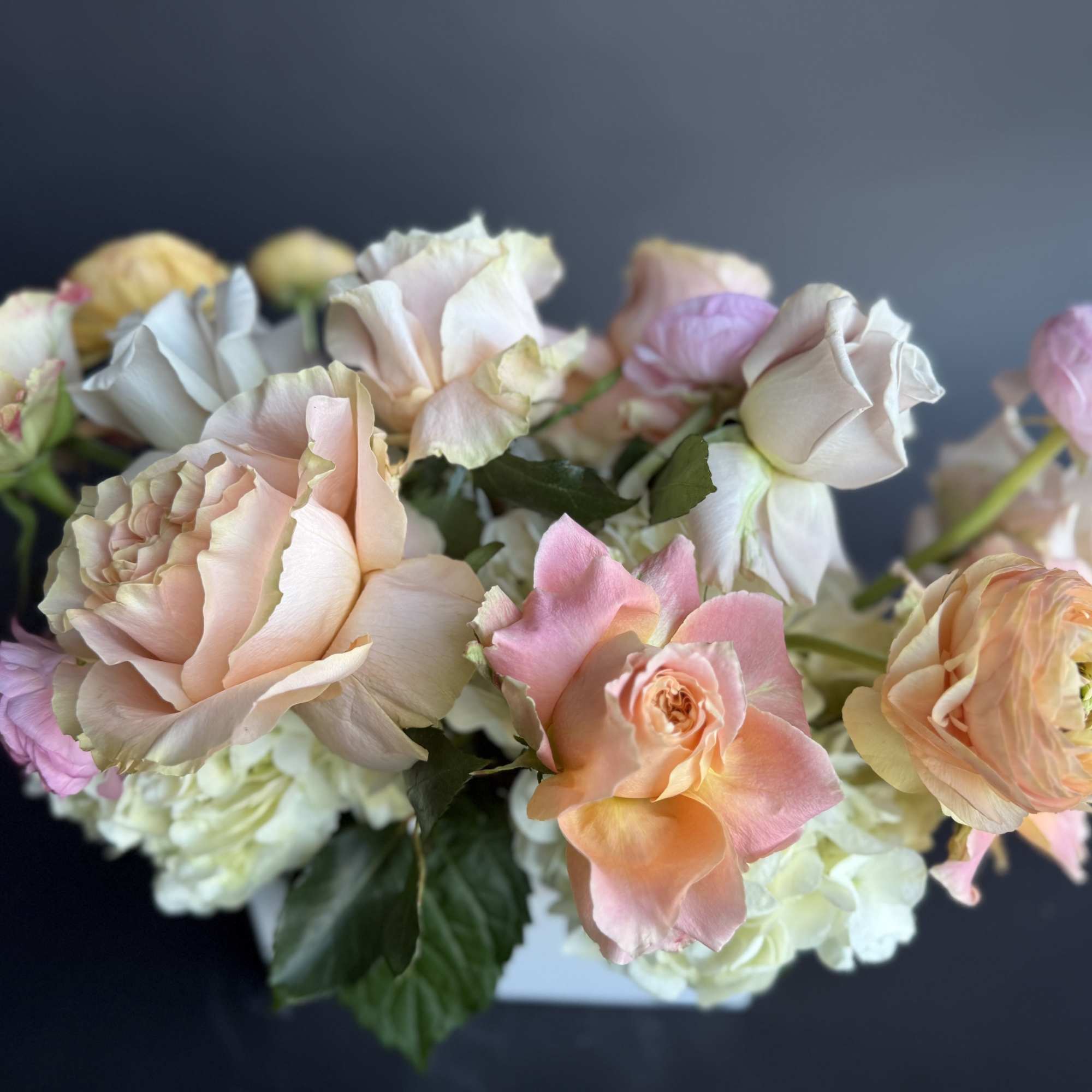 Low arrangement of pastel roses and ranunculus in a white rectangular vase