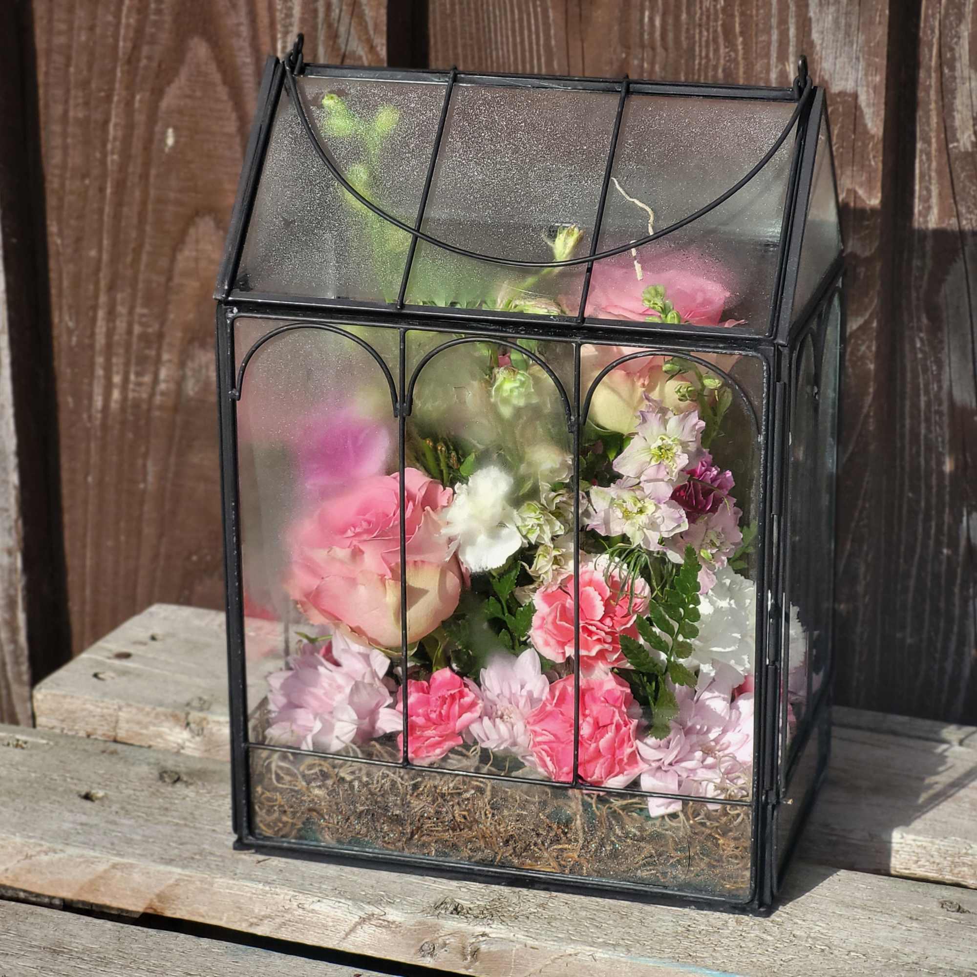 Pink and white flowers arranged inside a black glass terrarium box