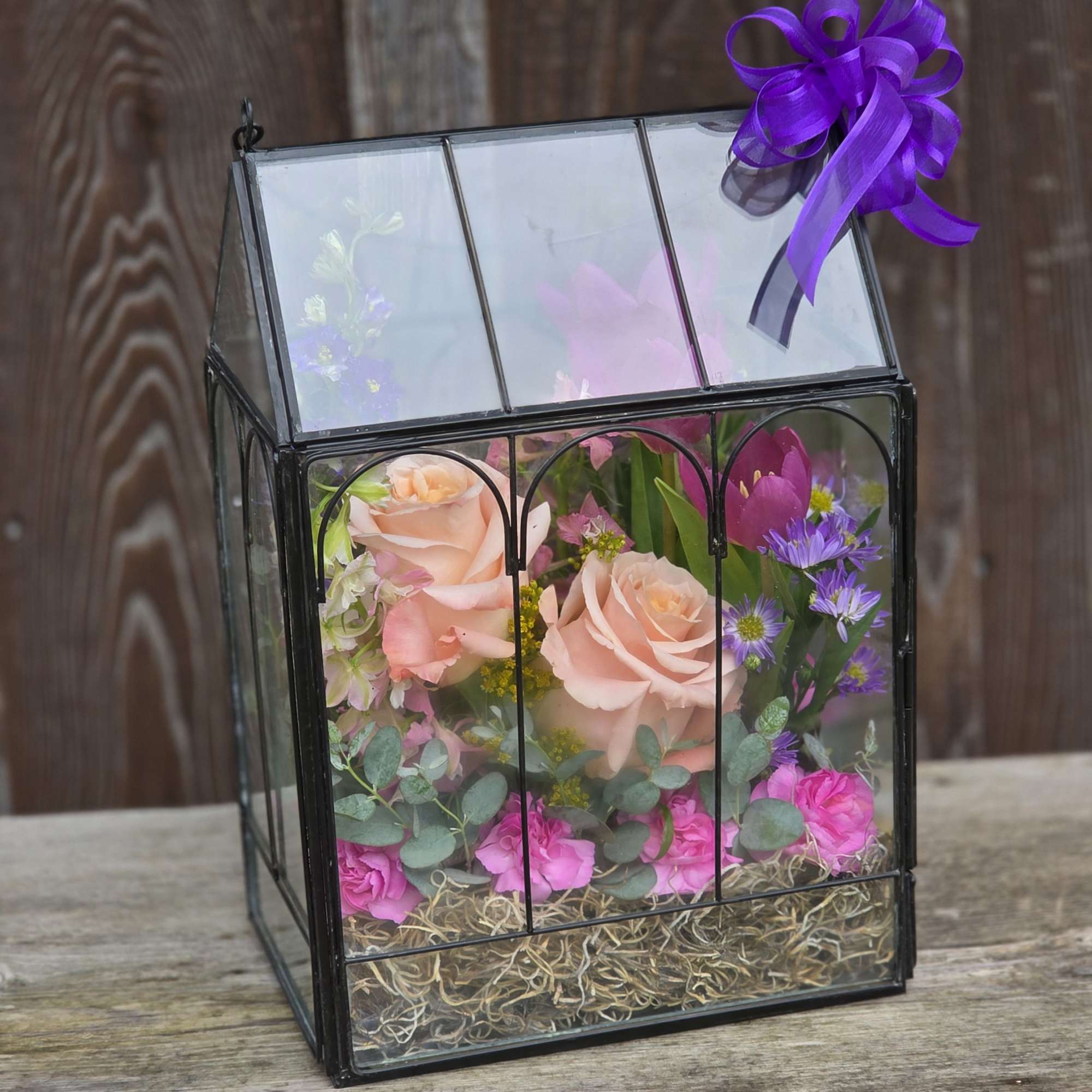 Floral arrangement in a glass lantern box with a purple ribbon bow