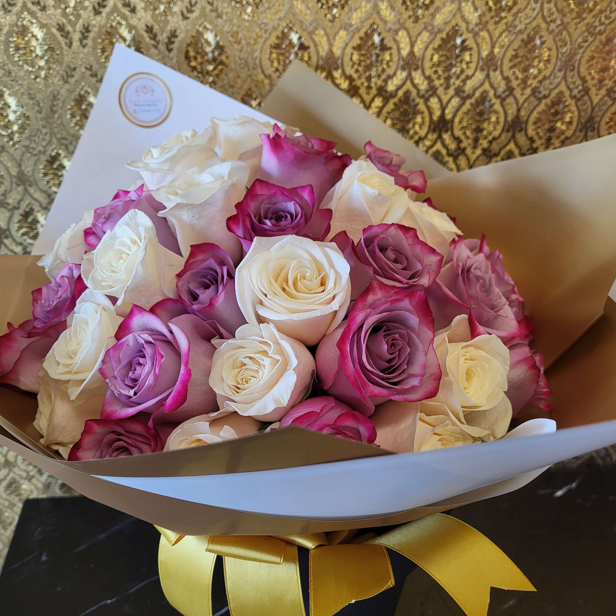 Bouquet of pink, purple, and white roses wrapped in paper with a yellow ribbon