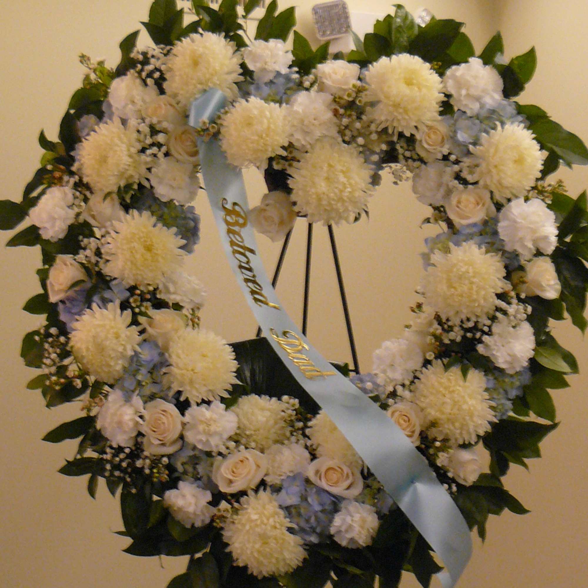 Heart-shaped funeral wreath with white flowers and a blue ribbon on an easel