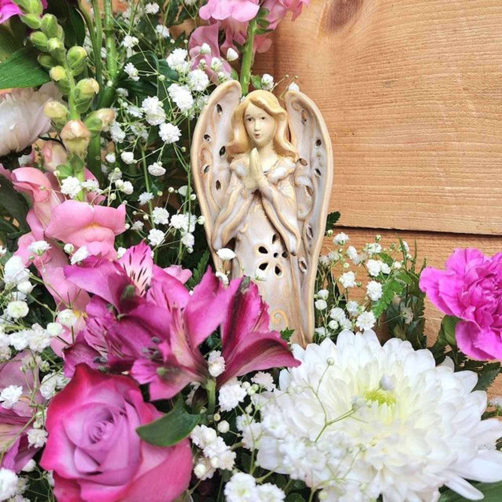 Pink and white flowers arranged around a small angel figurine
