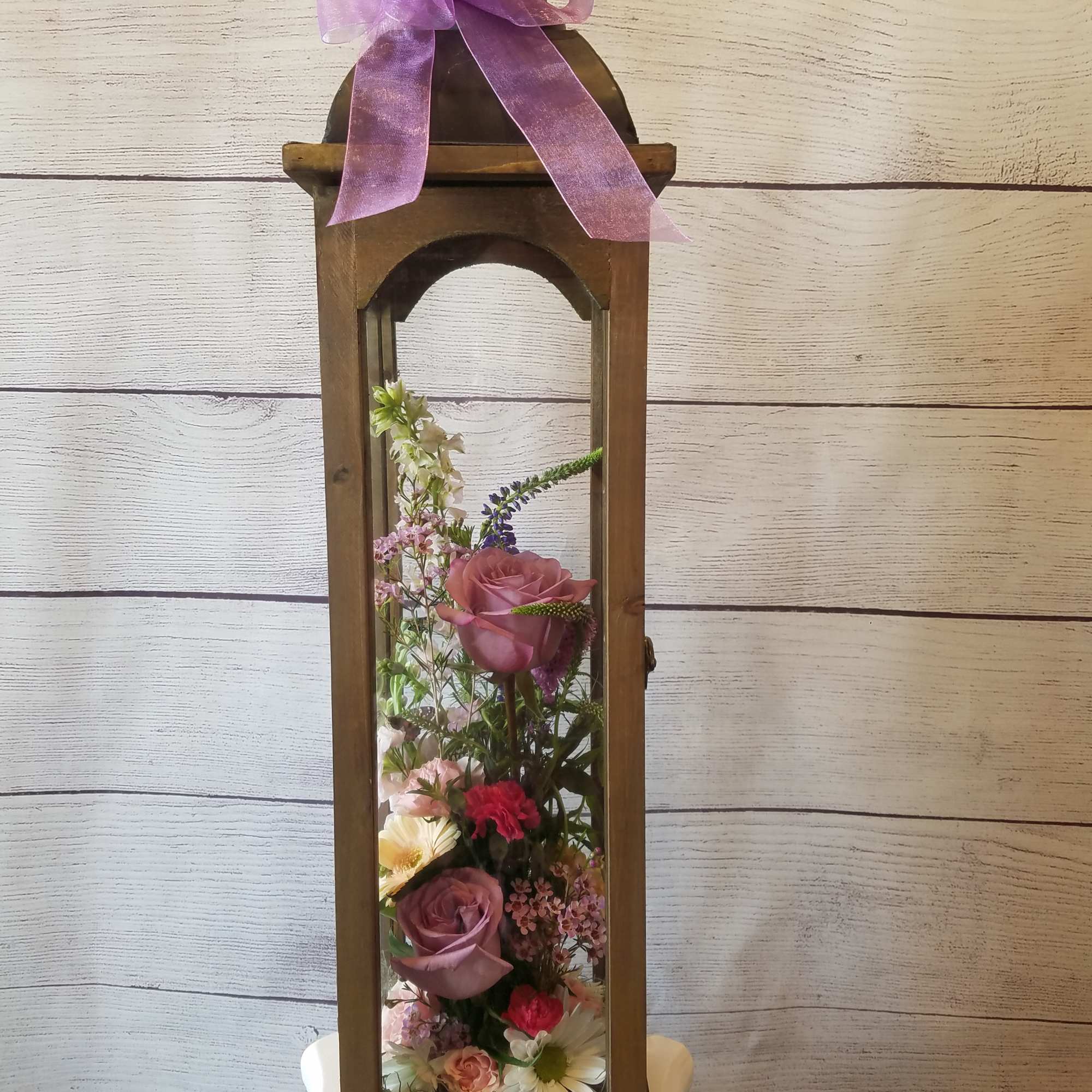 Tall wooden lantern with a pink ribbon and mixed flowers inside