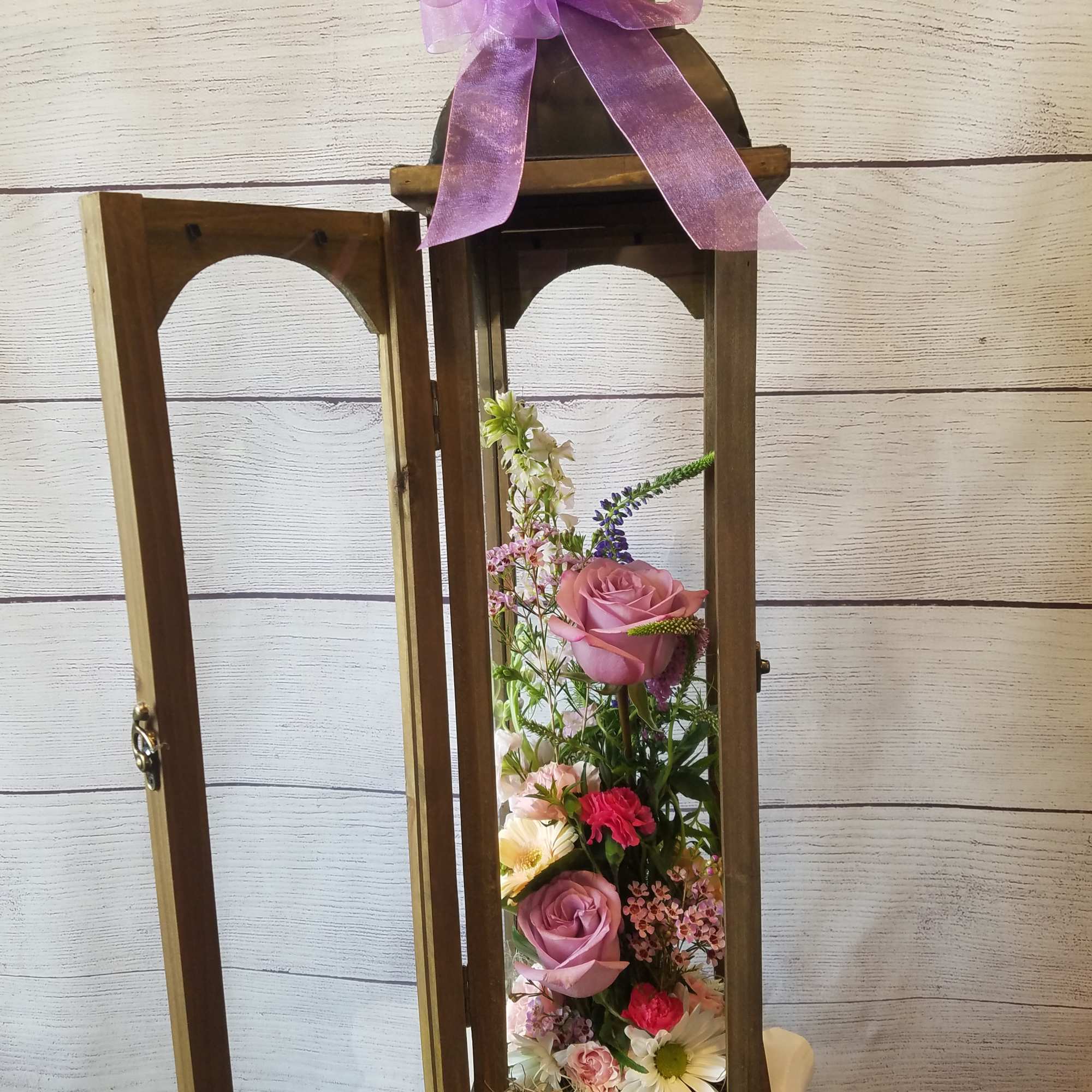 Wooden lantern with a pink ribbon and mixed flowers inside