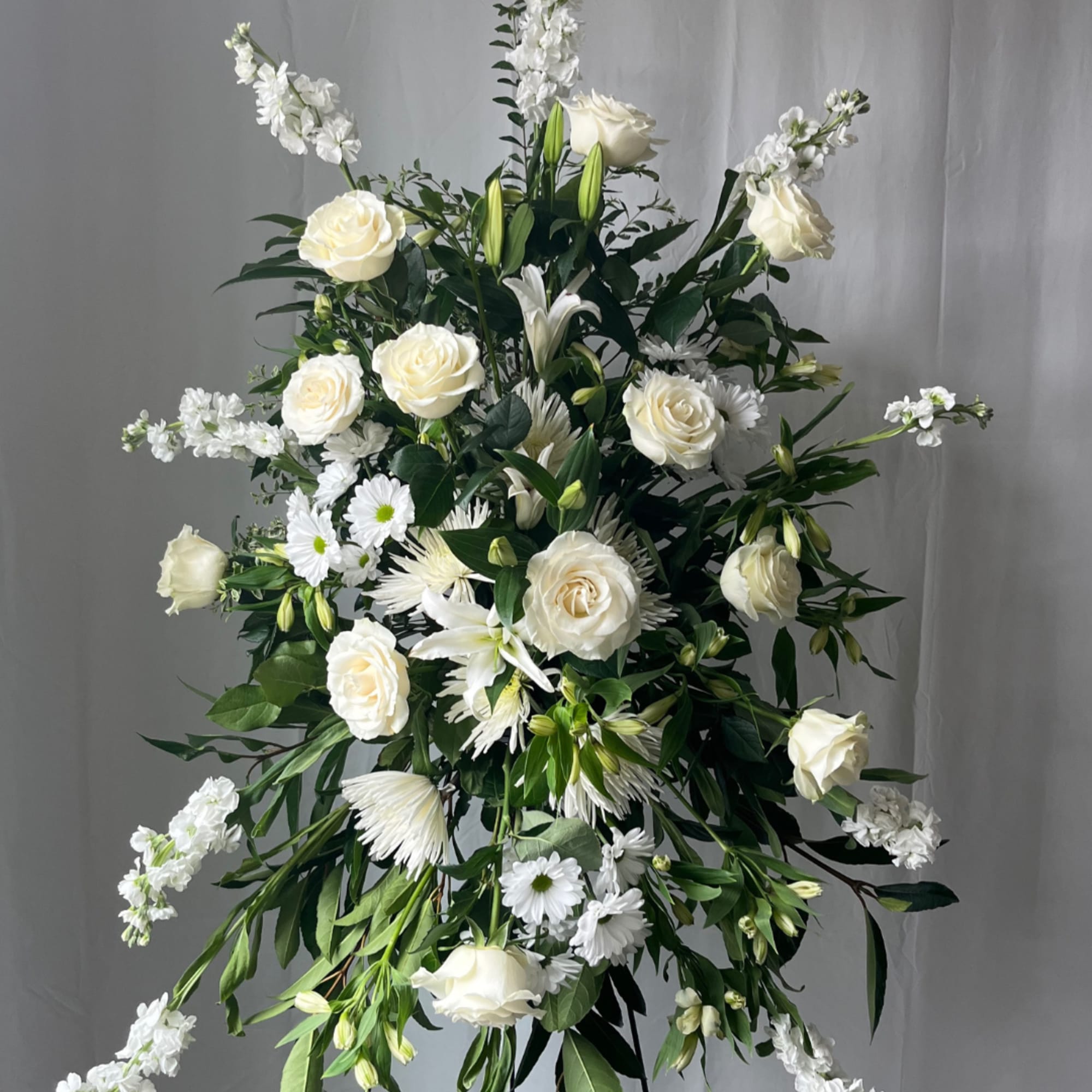 Tall white floral standing spray with roses and daisies on a black easel