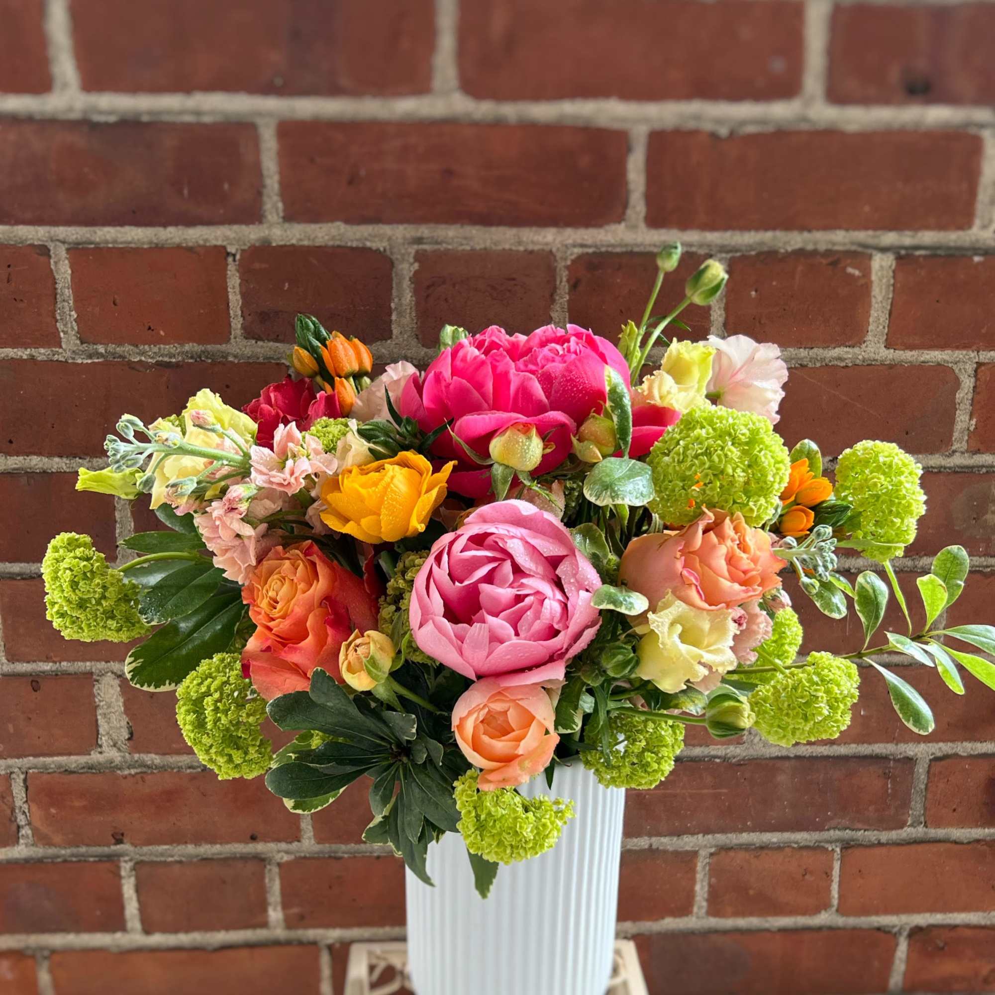 Bright mixed bouquet of pink peonies and orange and yellow blooms in a tall white vase