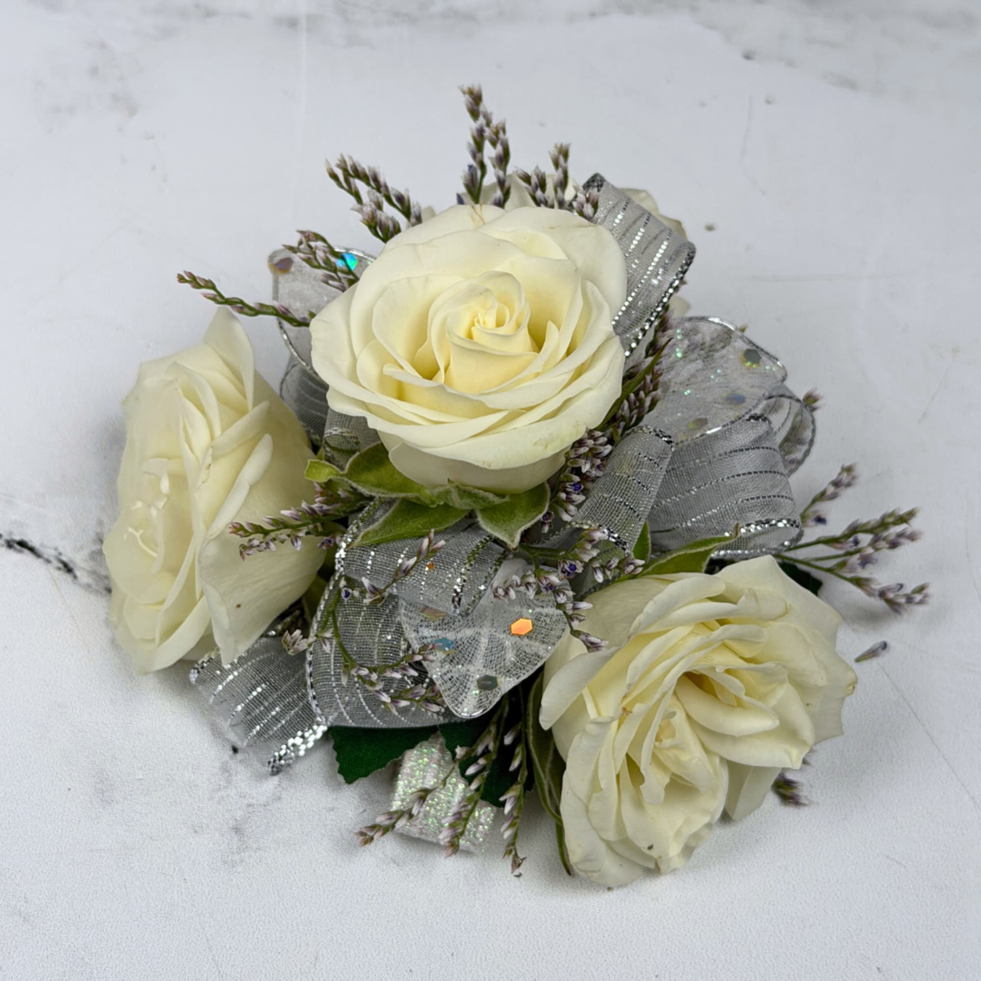 Three cream-white roses gathered into a compact wrist corsage create a quietly