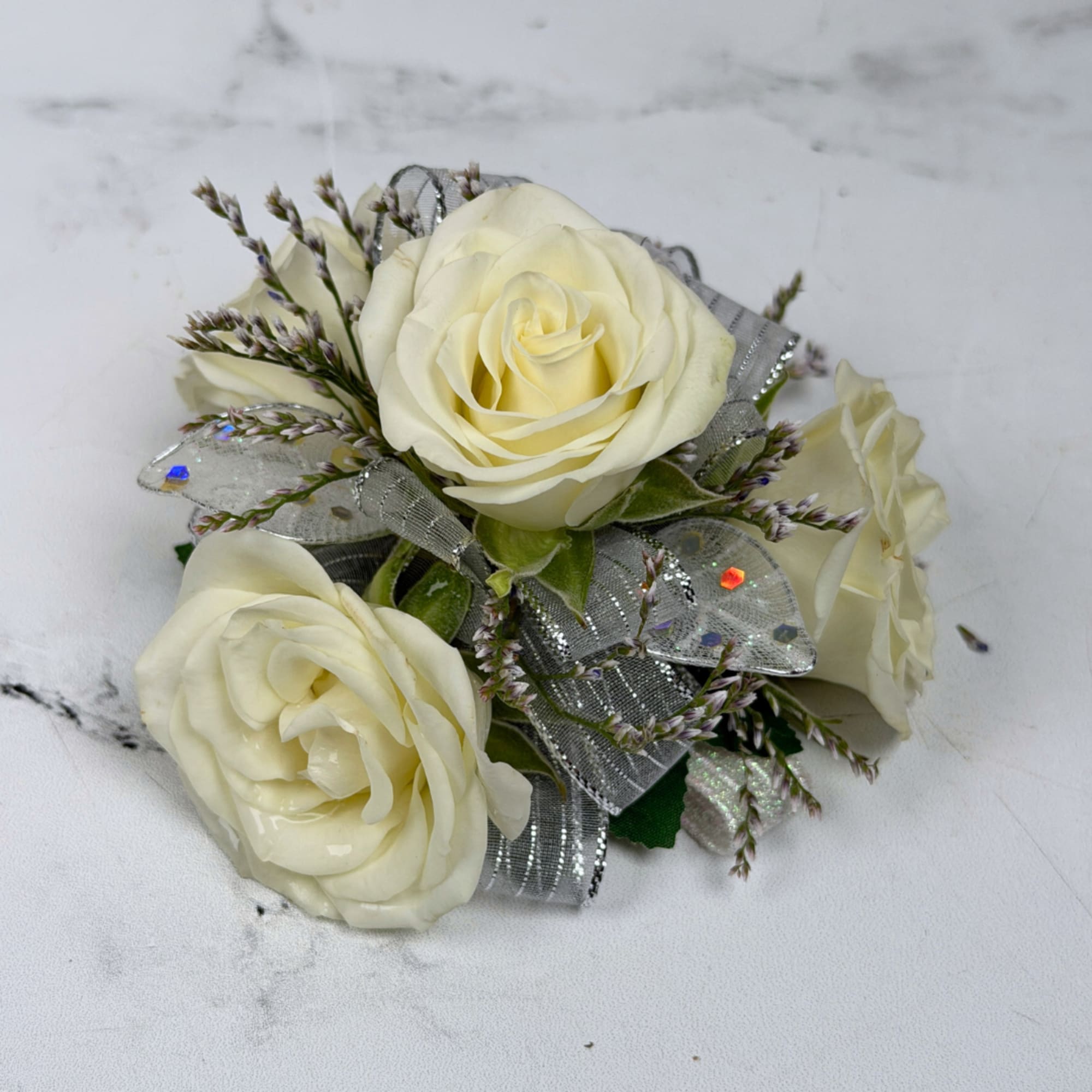 Three cream-white roses gathered into a compact wrist corsage create a quietly