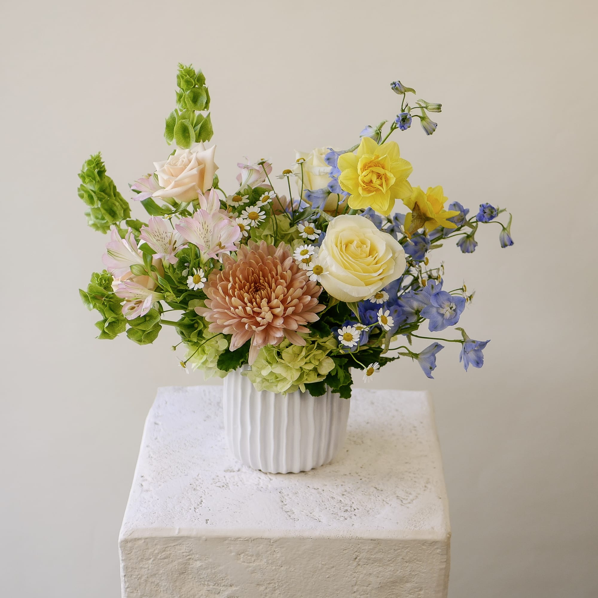 Pastel arrangement of daffodils, roses, chrysanthemum and mixed flowers in a white ribbed vase
