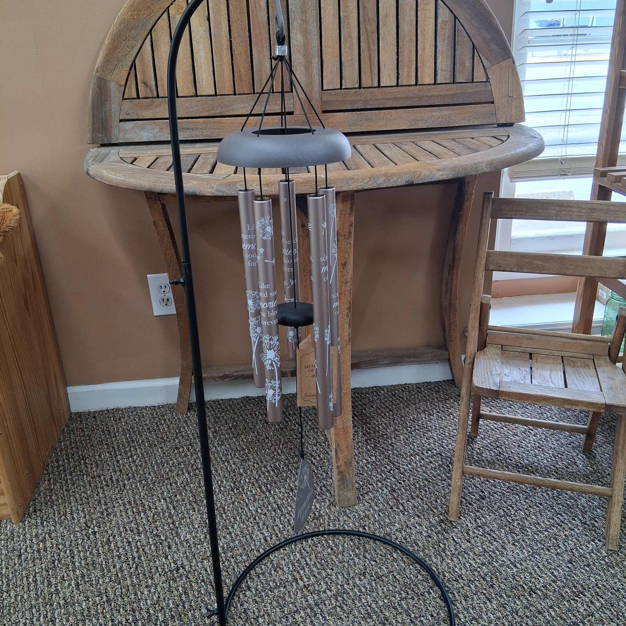 Black metal wind chime hanging in front of a wooden table and chair